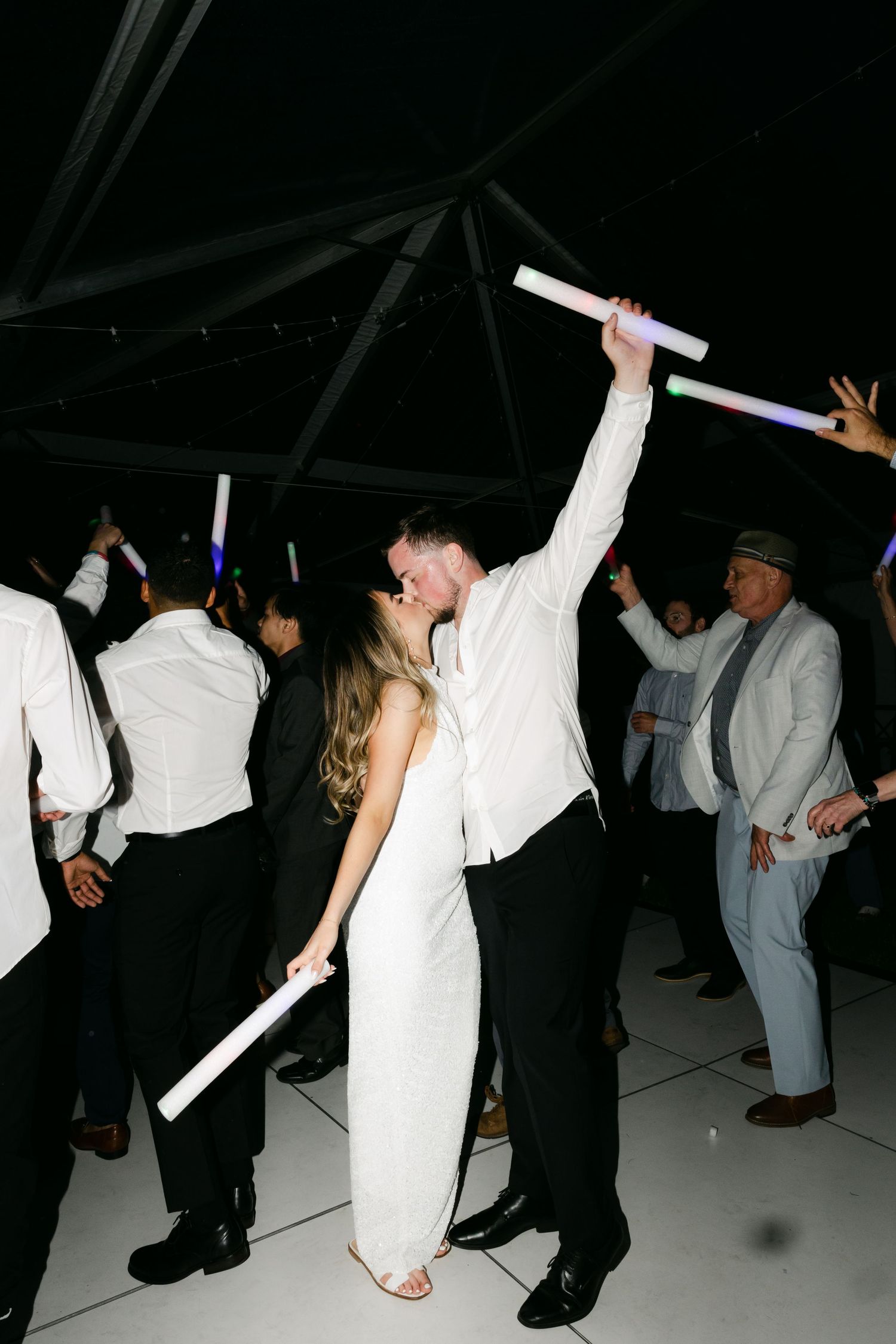 Wedding guests dancing and celebrating on a dark dance floor with glowing lights.