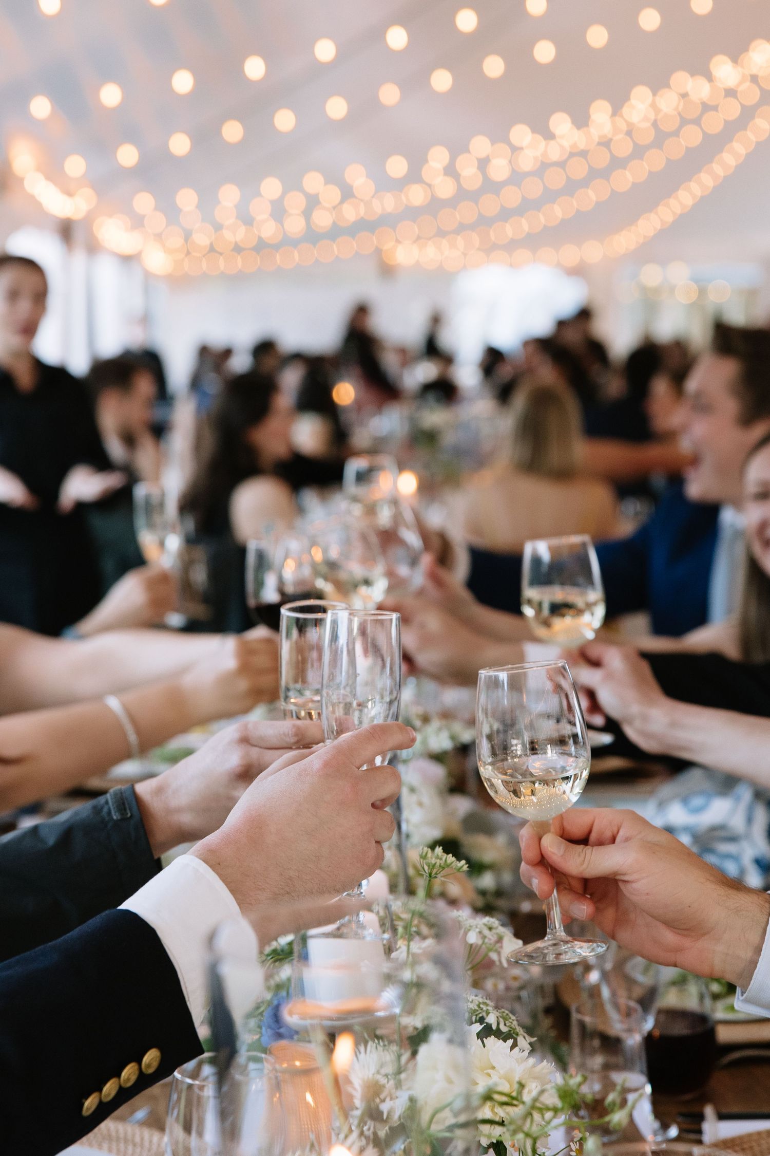 Wedding guests raising glasses of white wine in a toast at an elegantly decorated reception table.