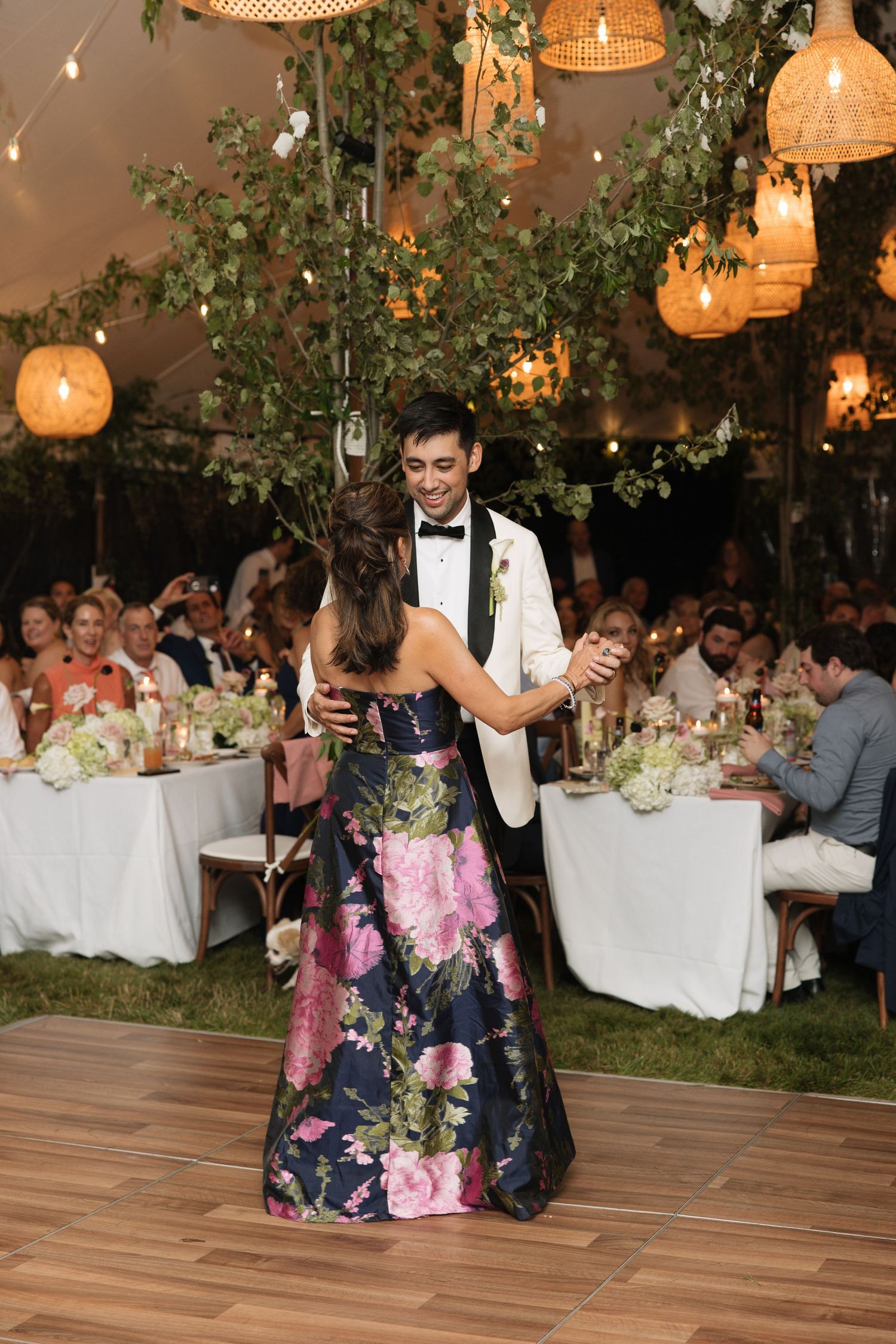 Couple shares first dance under glowing lanterns and greenery at elegant outdoor tented wedding reception.