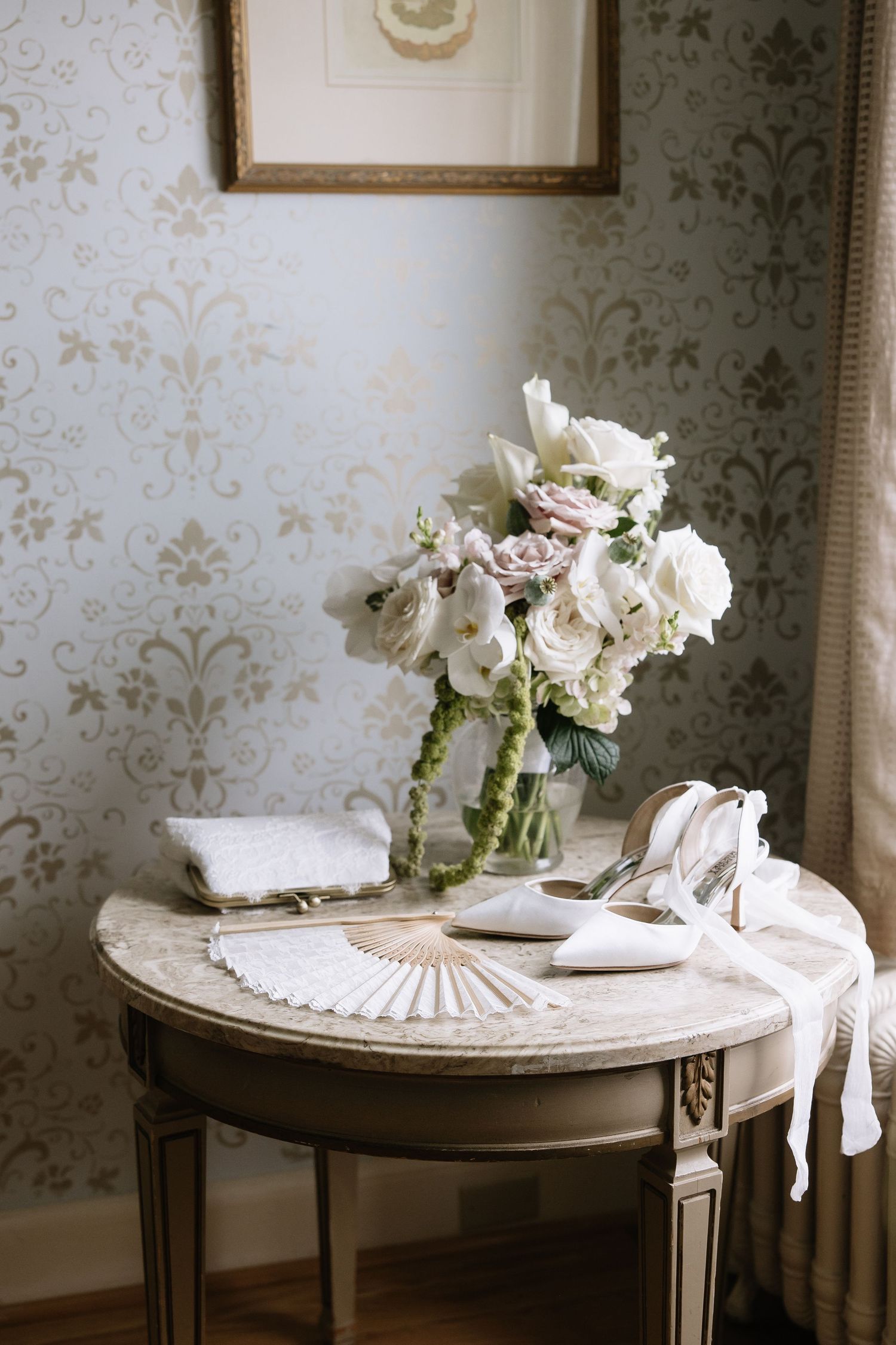 Elegant white floral arrangement with bridal accessories on vintage round table.