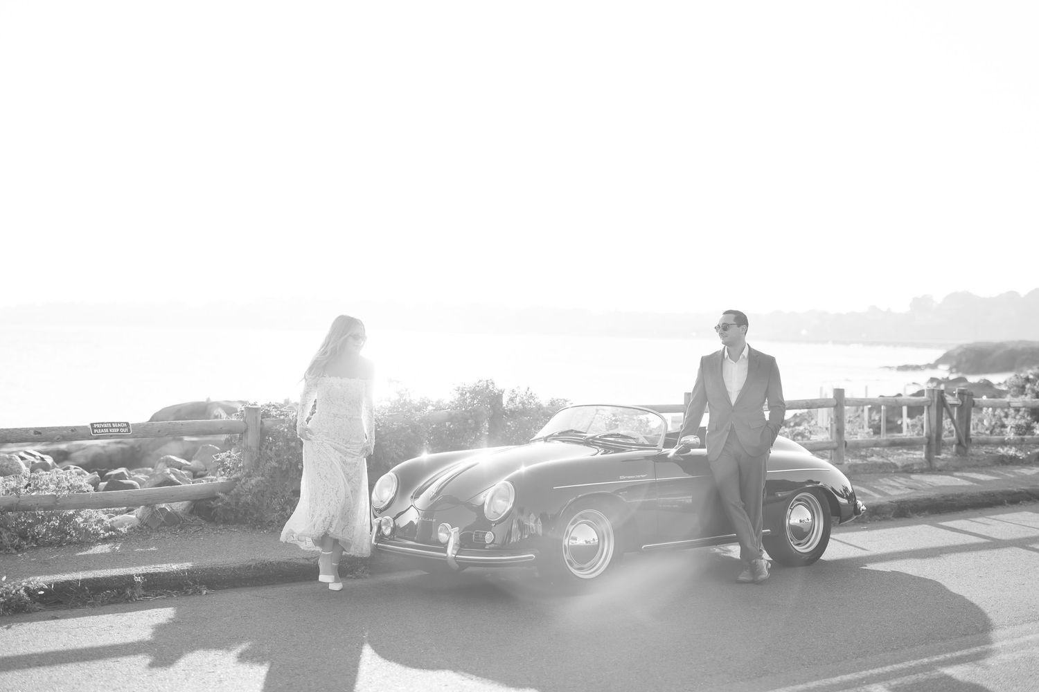 A panoramic black and white view of a vintage car parked along a scenic overlook.
