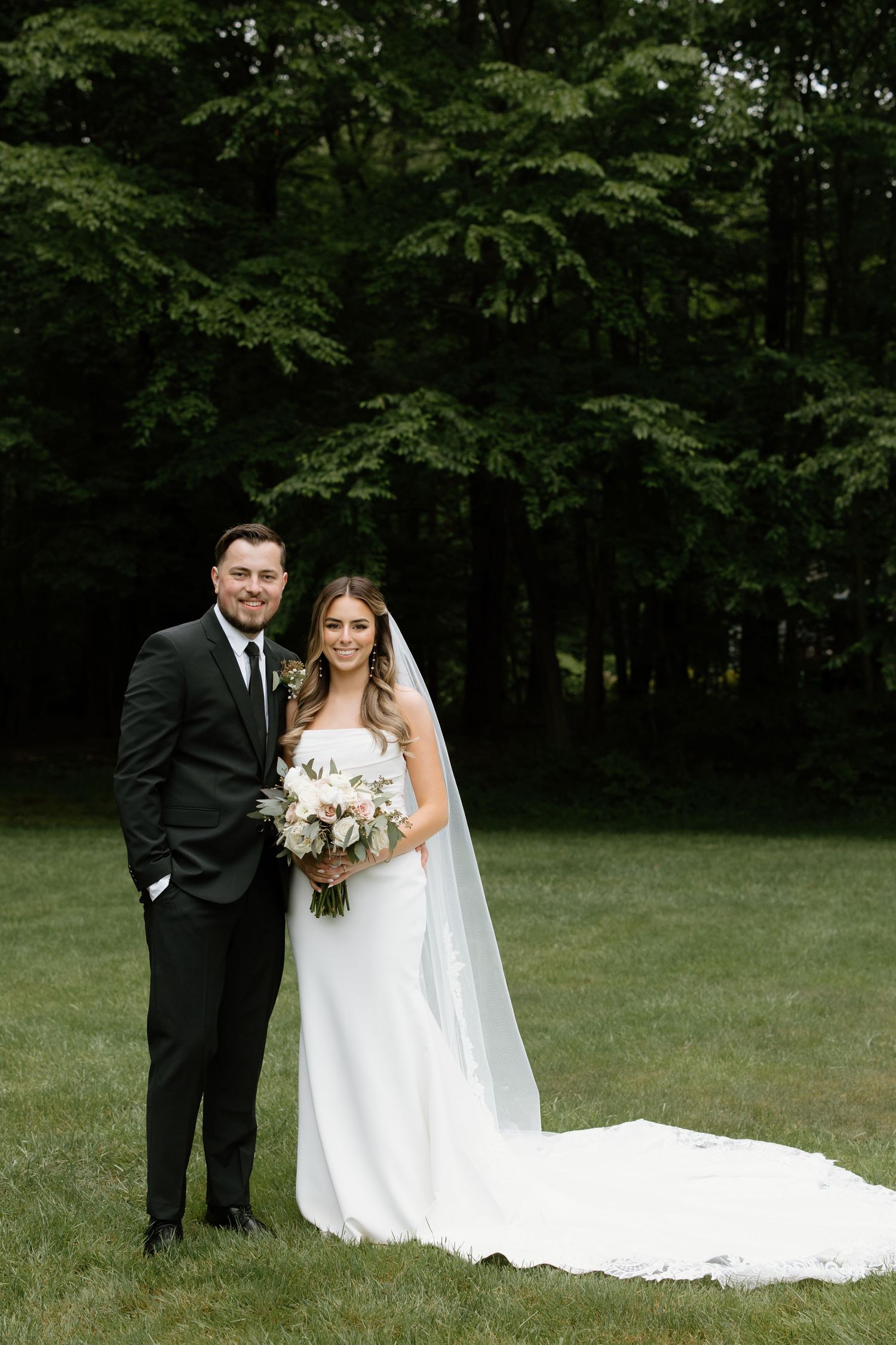 Elegant outdoor wedding portraits in a lush green field with flowing white dress and dark suit.