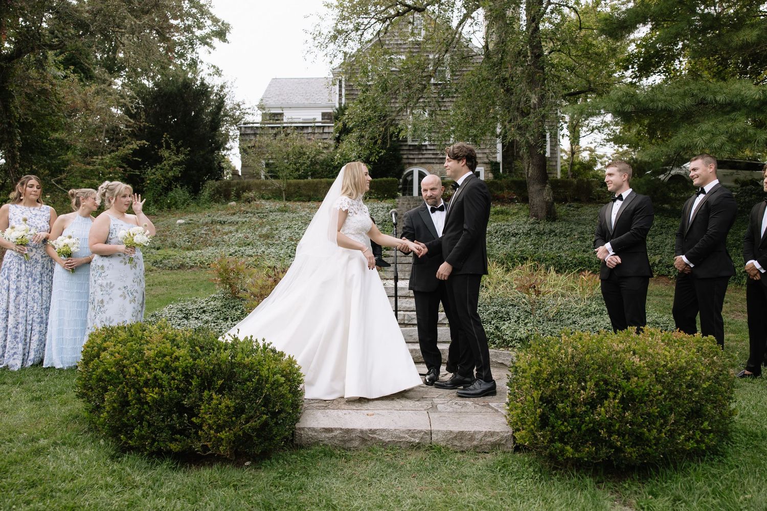 Wedding ceremony on garden path with bridal party in formal attire.