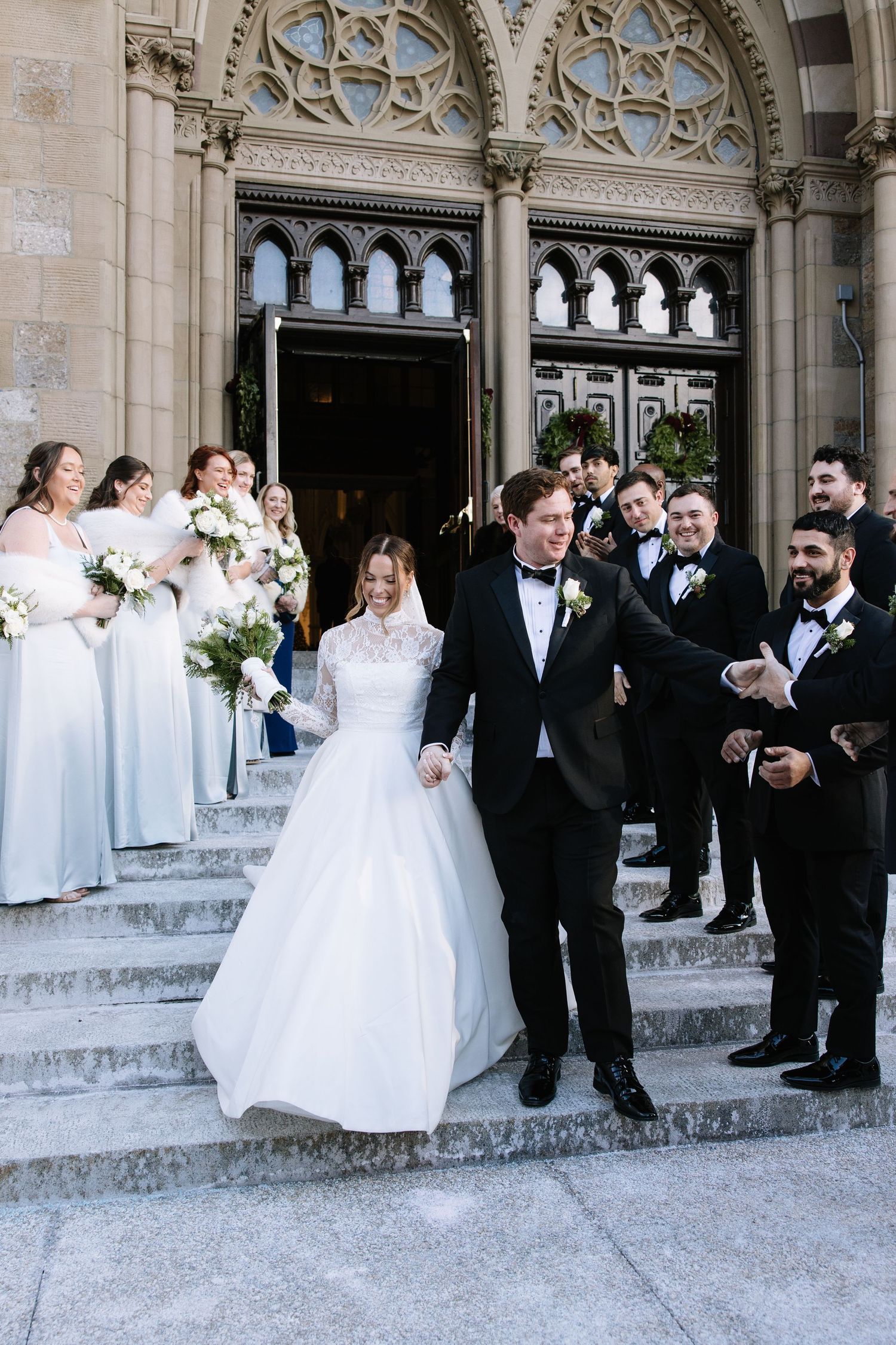 Wedding party gathered on stone steps outside a Gothic church entrance.
