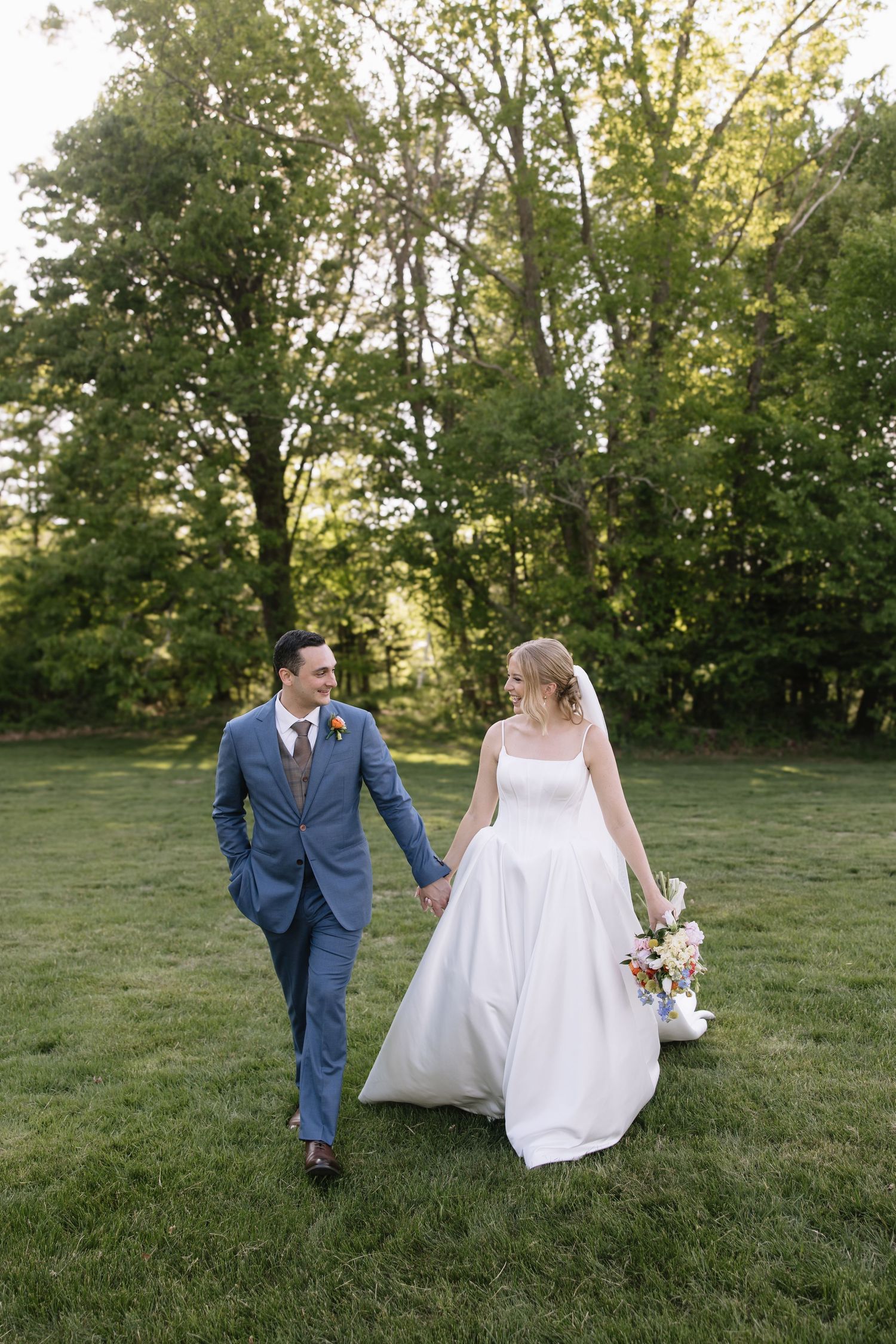 Couple walking through a sunlit meadow during their wedding photoshoot.