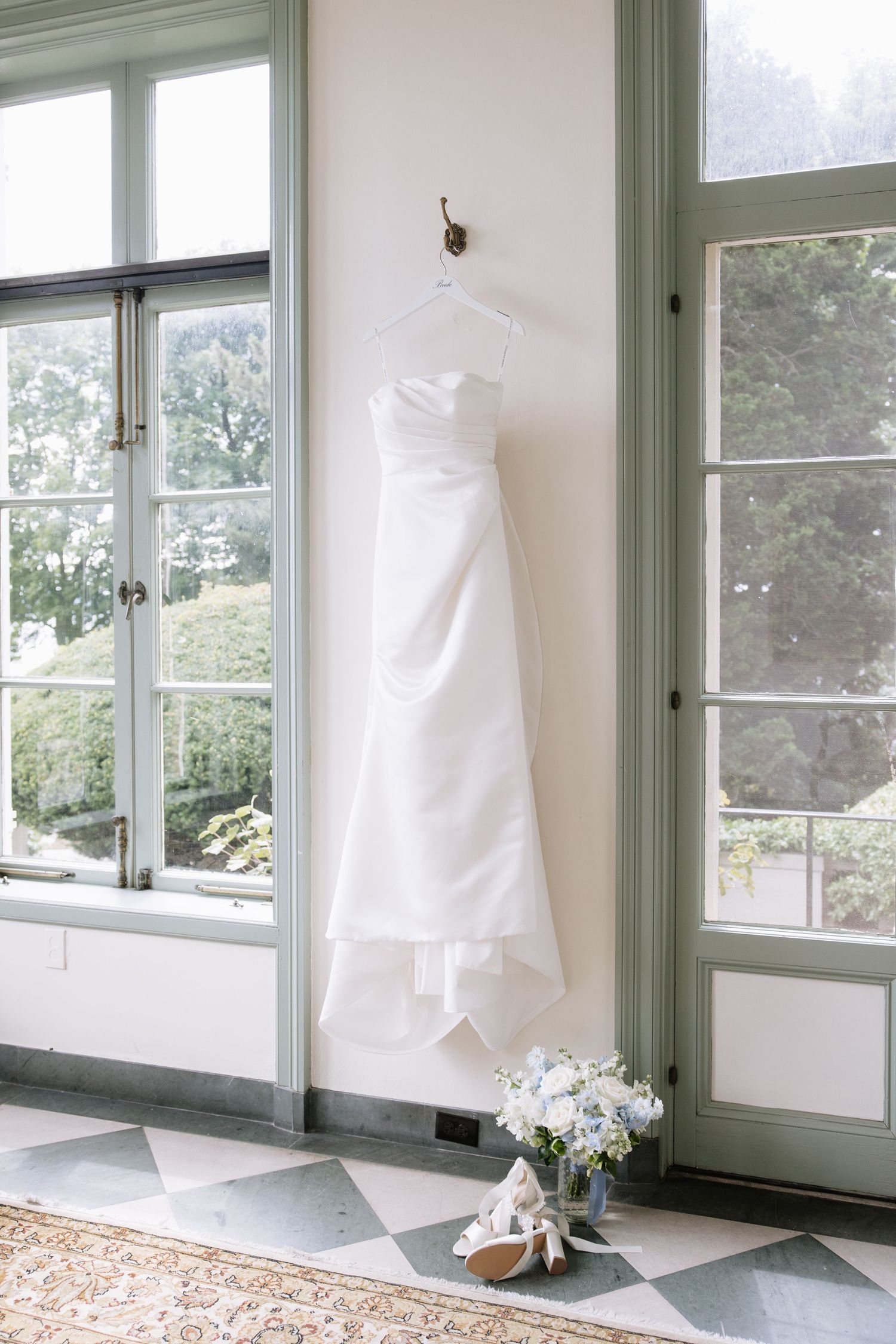 Sunlit room with green-trimmed windows displays white wedding dresses hanging by the windows.