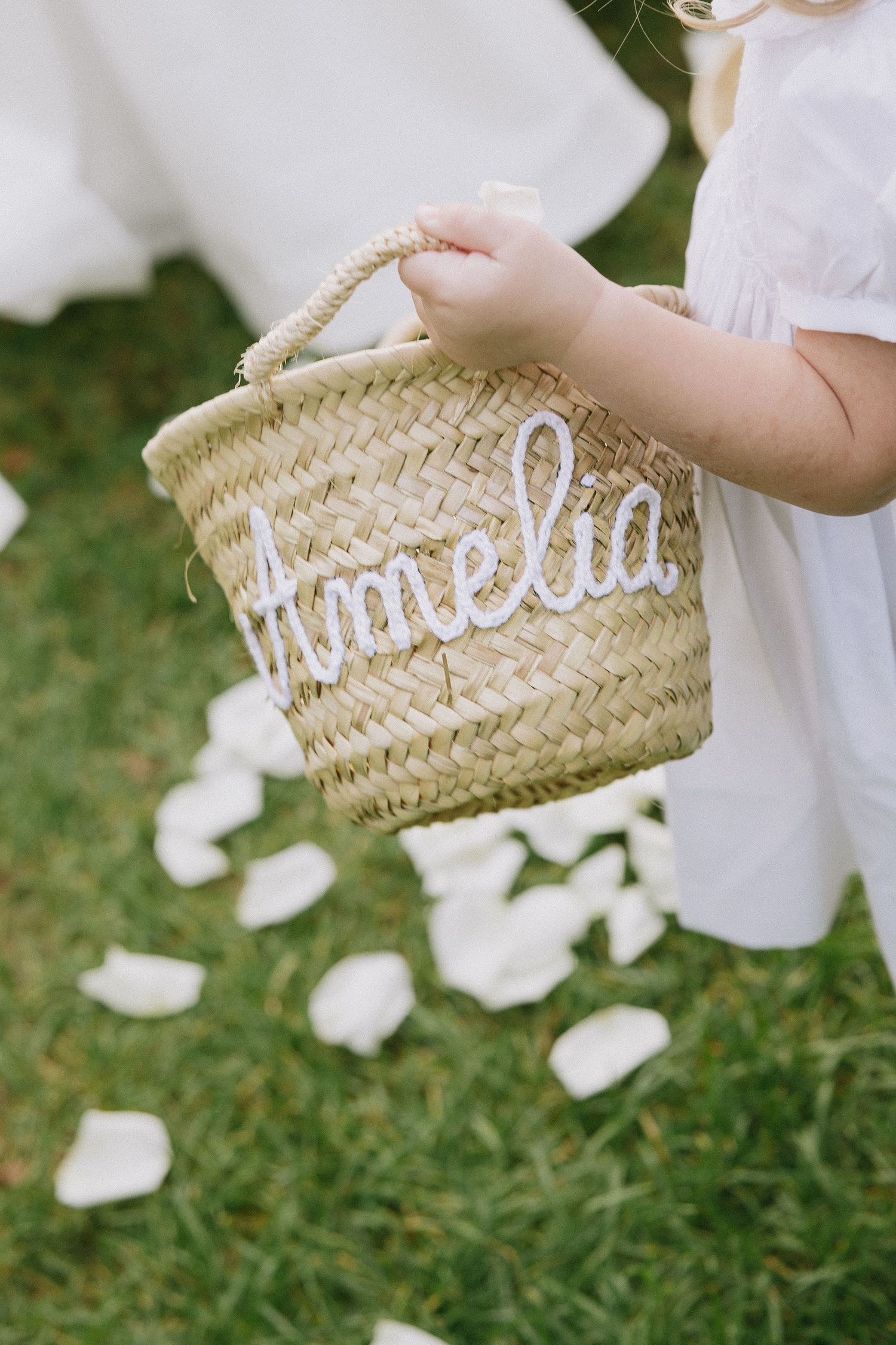 Decorative woven basket with white lettering displayed on grass with scattered flower petals.