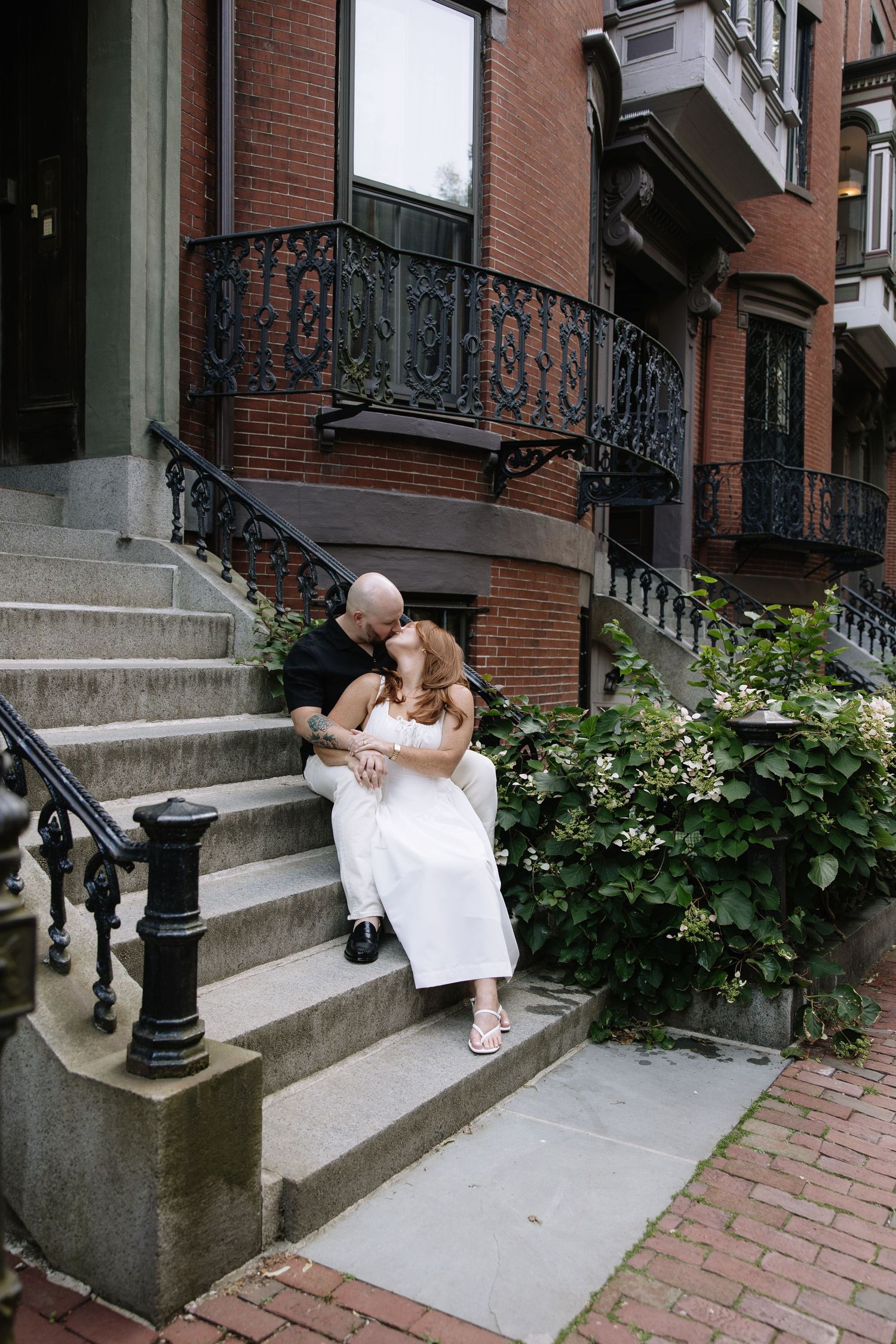 Couple sitting on brick building steps with ornate iron railings.
