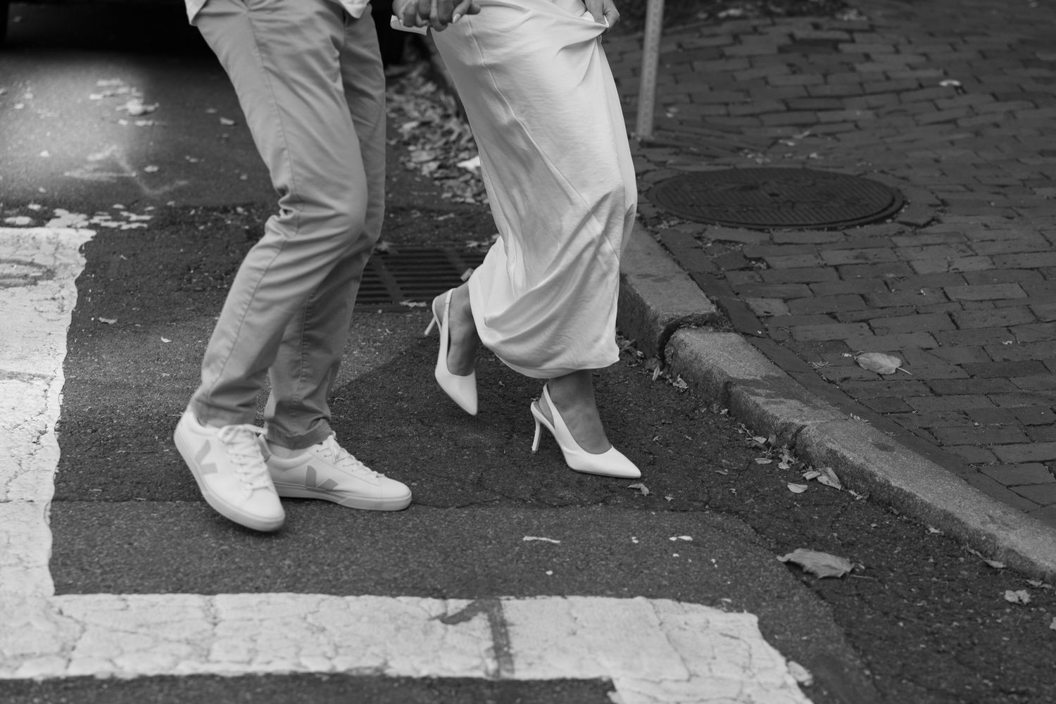 Black and white detail shot of two pairs of feet in formal shoes on cobblestone pavement.