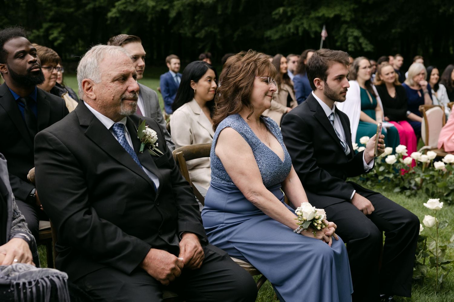 Wedding guests seated outdoors watching the ceremony among floral decorations.