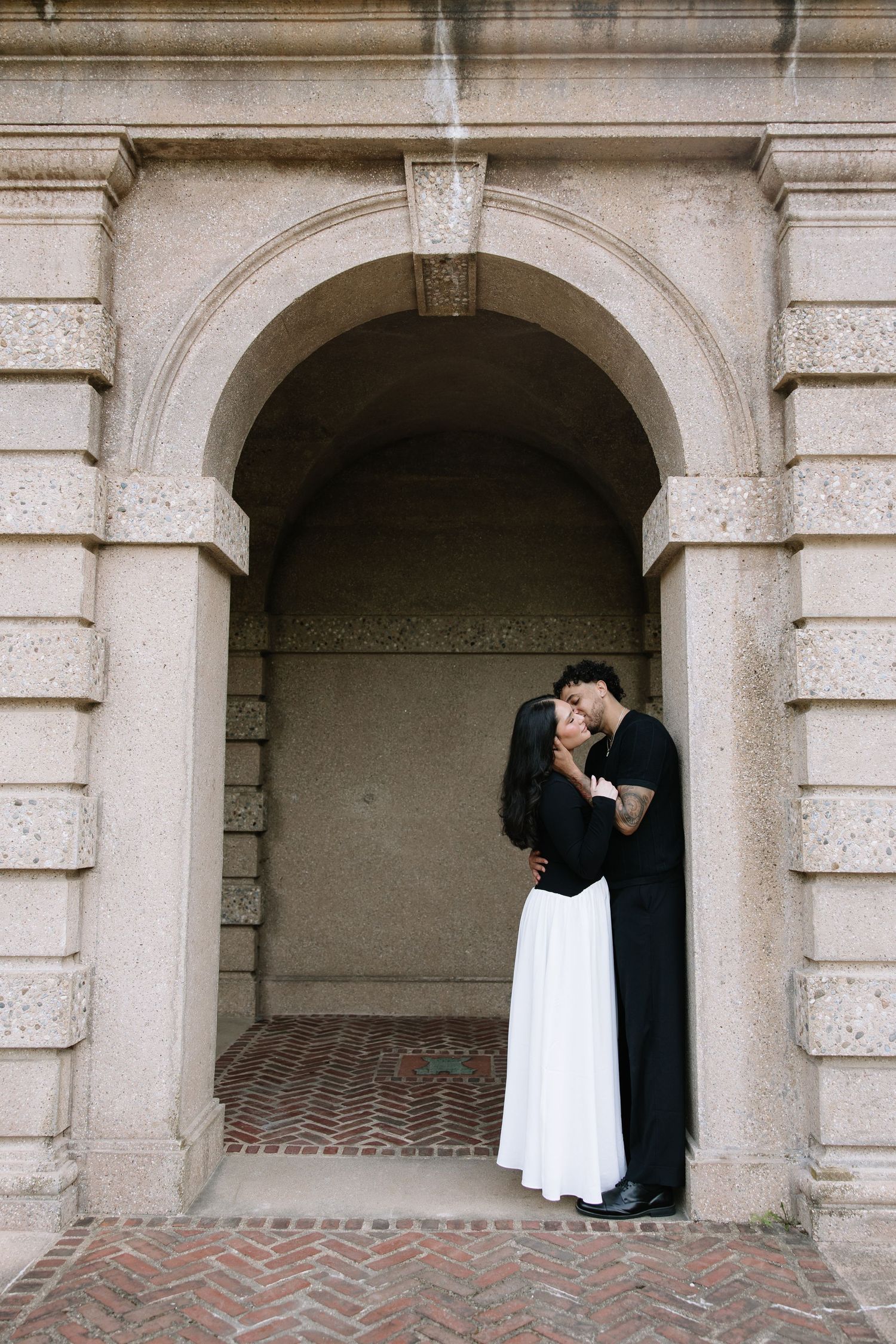 An intimate portrait beneath a classical stone archway with herringbone brick floor.
