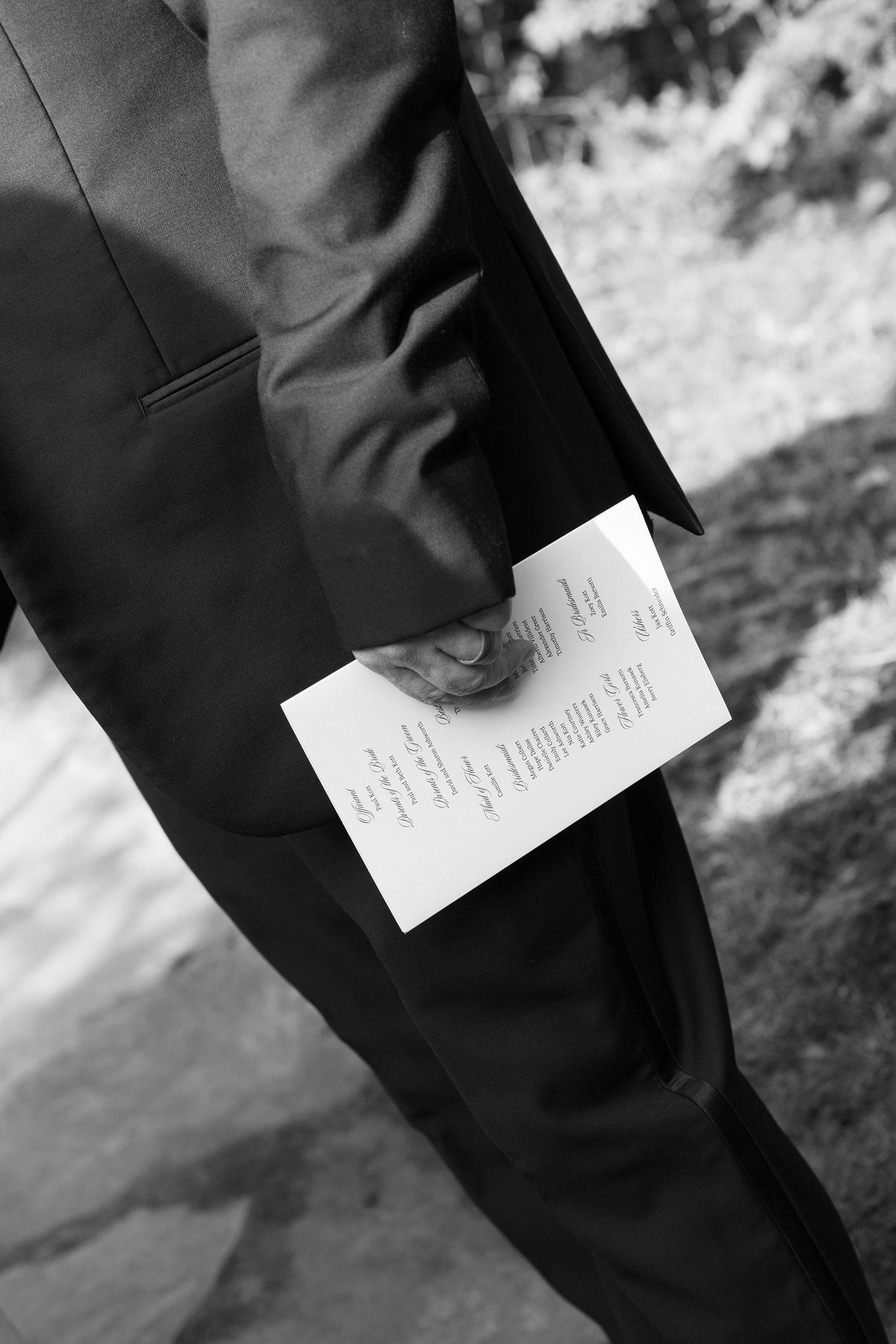 Black and white detail shot of wedding invitation being held in formal attire.