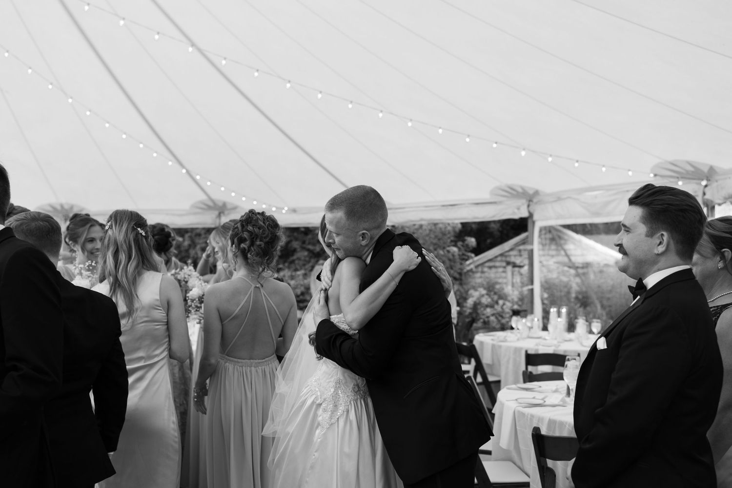 Wedding reception guests gather under an elegant white tent for evening celebrations.