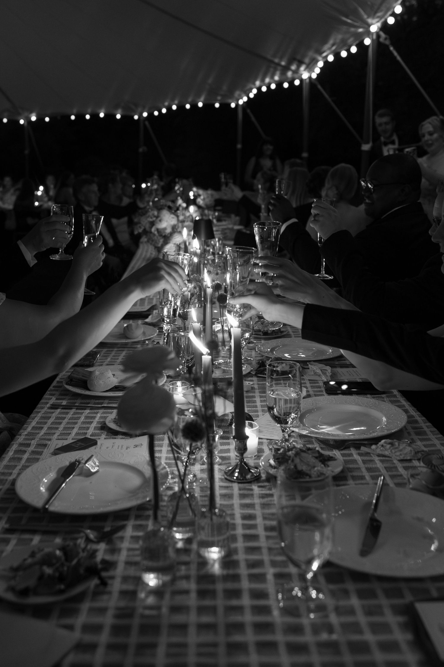 Guests raising glasses in a toast at elegant candlelit wedding reception under a tent.