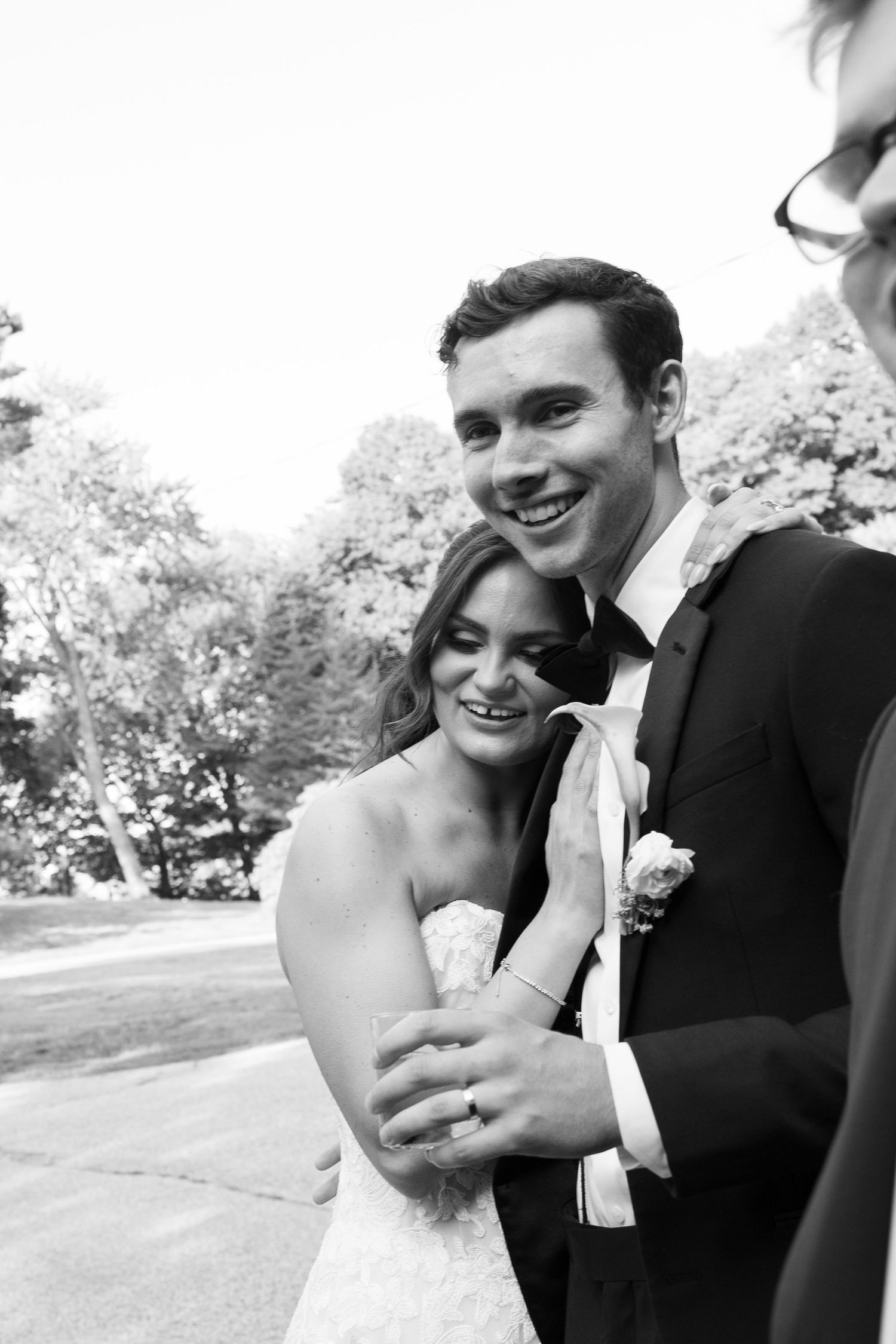 Black and white photo of a smiling bride and groom embracing outdoors on their wedding day.