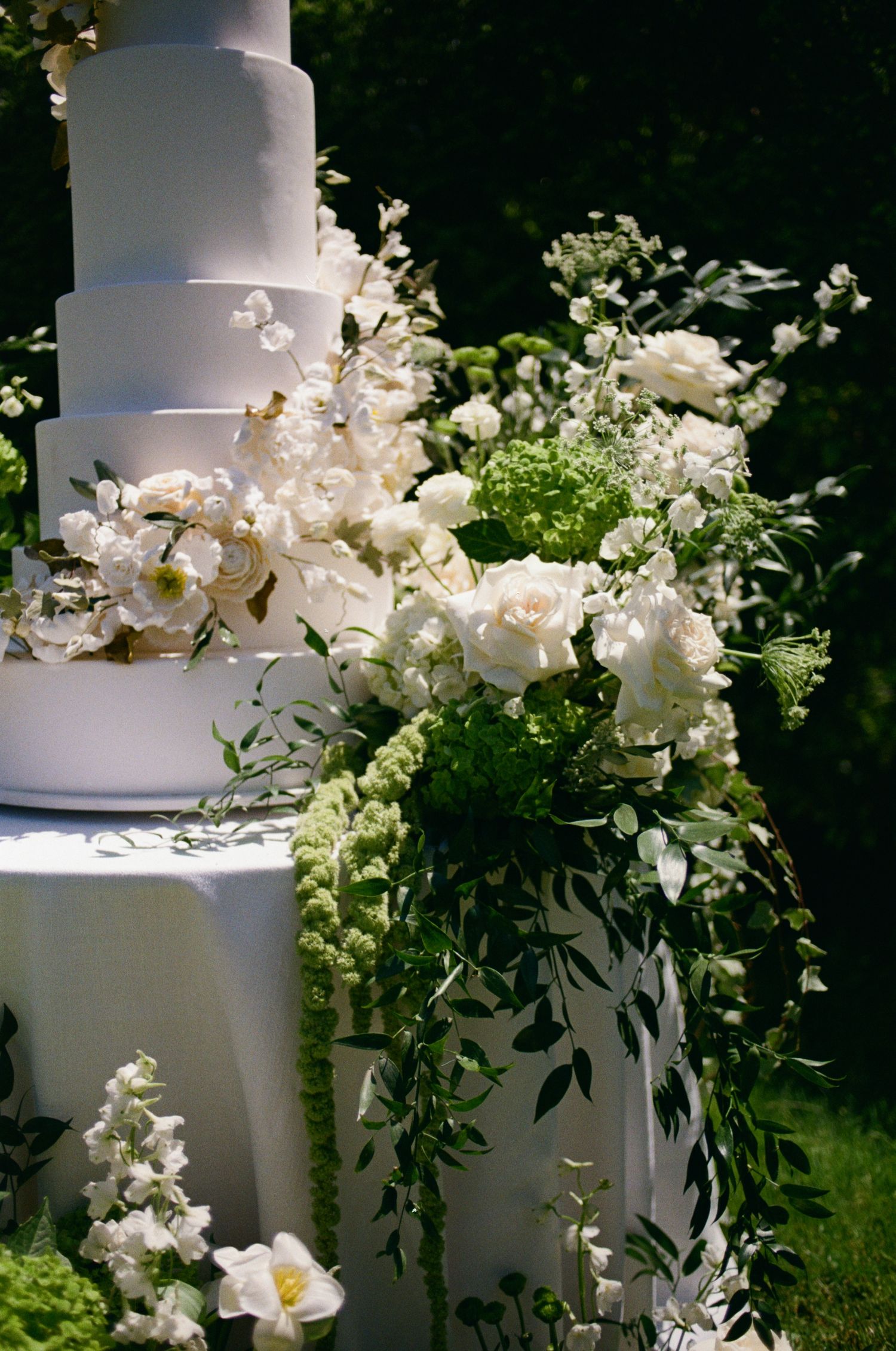 Close-up detail of a white tiered wedding cake decorated with fresh white flowers and green foliage.