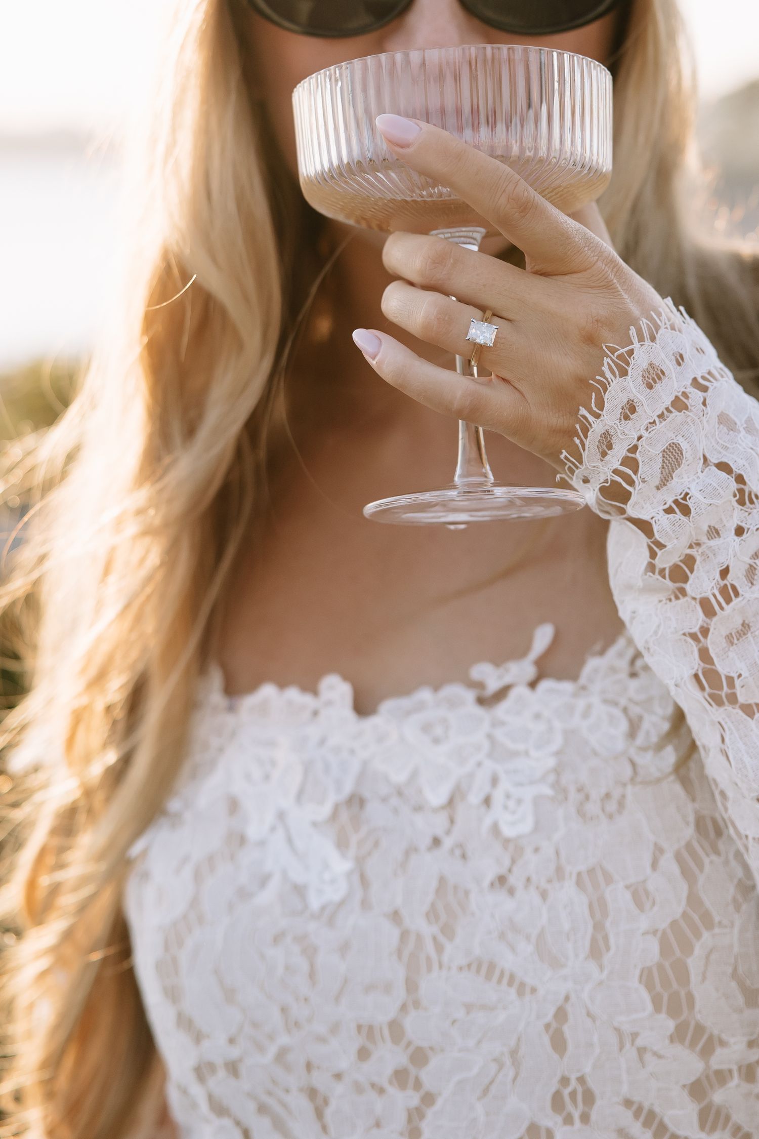 Close-up of lace sleeve and champagne glass with engagement ring detail.