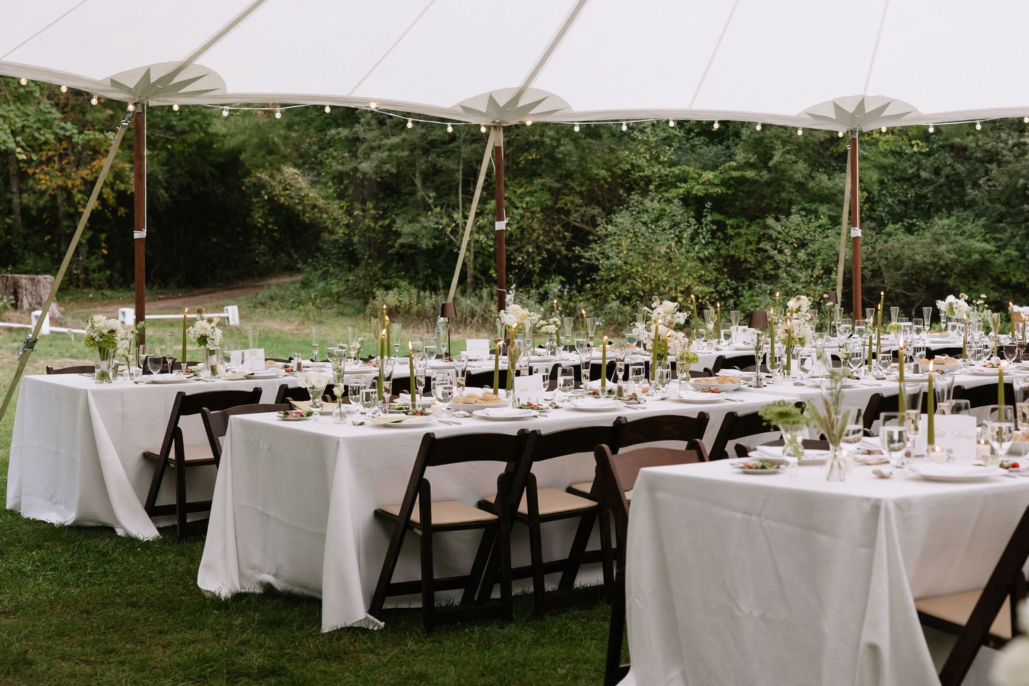 Large white tent set up on grass with elegant table settings for wedding reception.