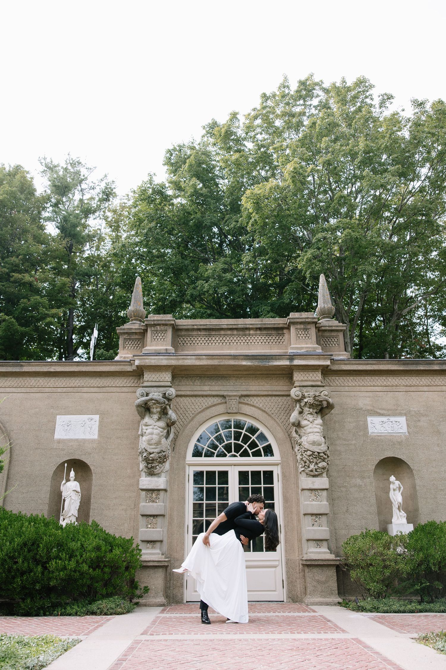 An ornate stone gateway entrance with classical architectural details and statuary in a garden setting.