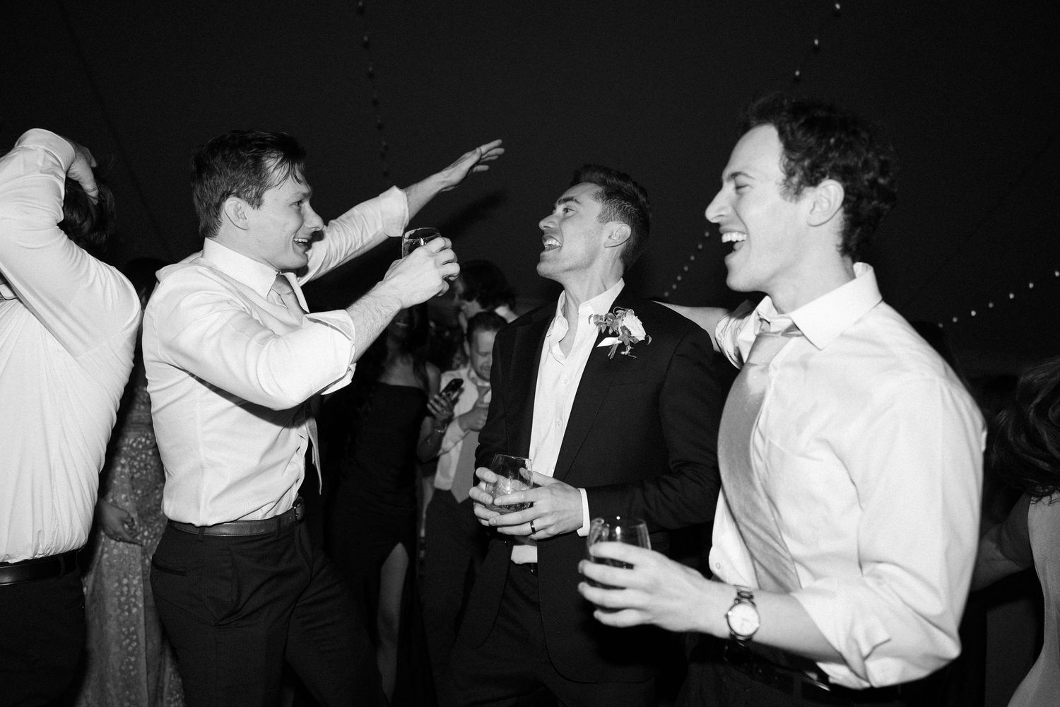 Groomsmen celebrating and dancing together in black and white photo at wedding reception.