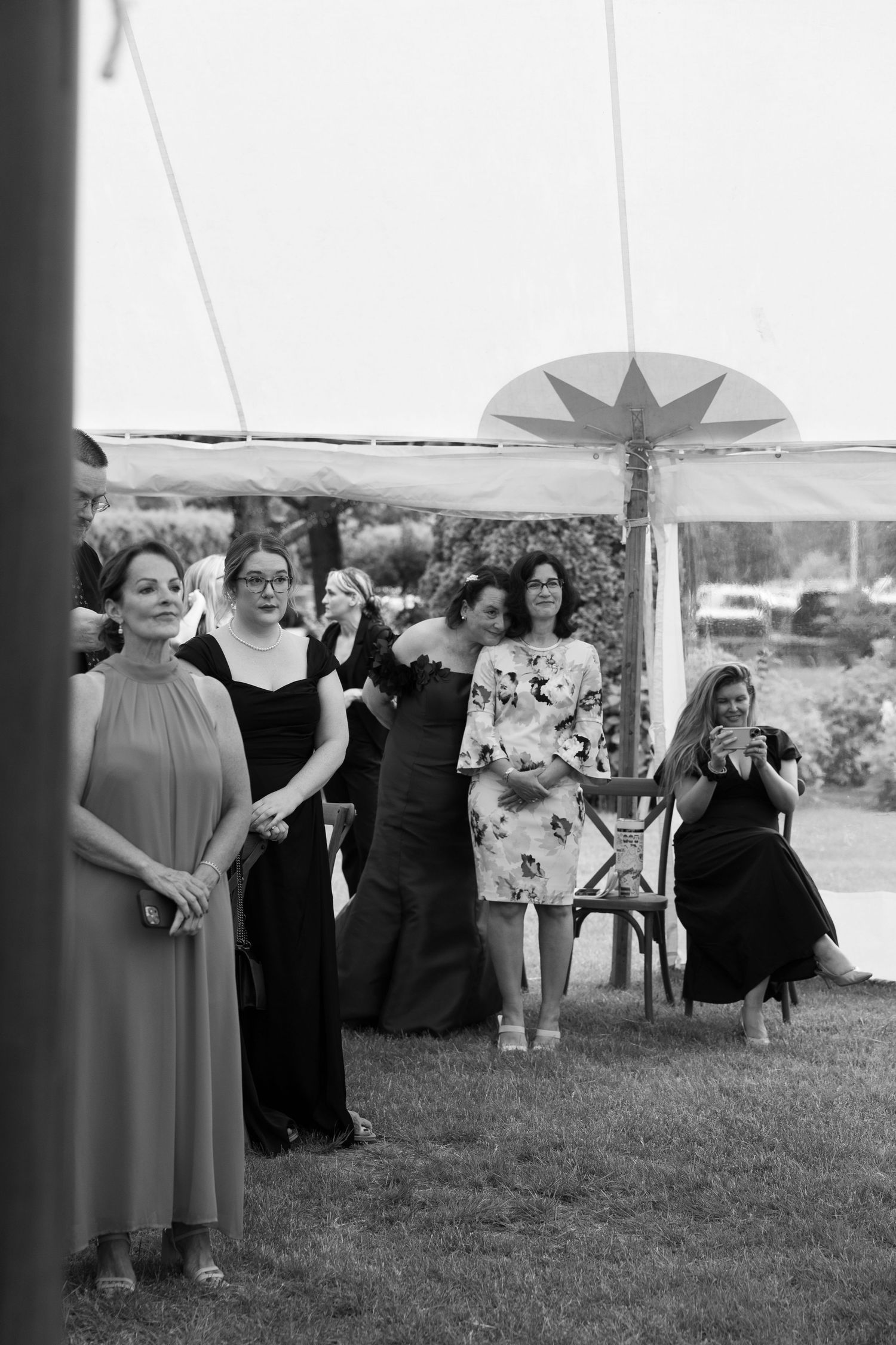 Black and white photo of elegantly dressed women gathered outdoors under a tent at a formal wedding event.