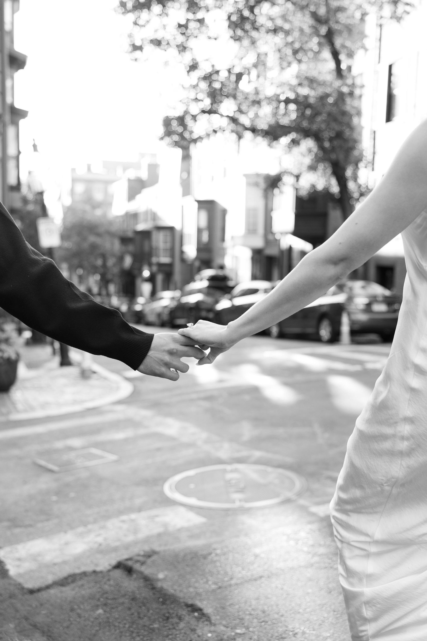 Black and white image of couple holding hands on urban sidewalk.