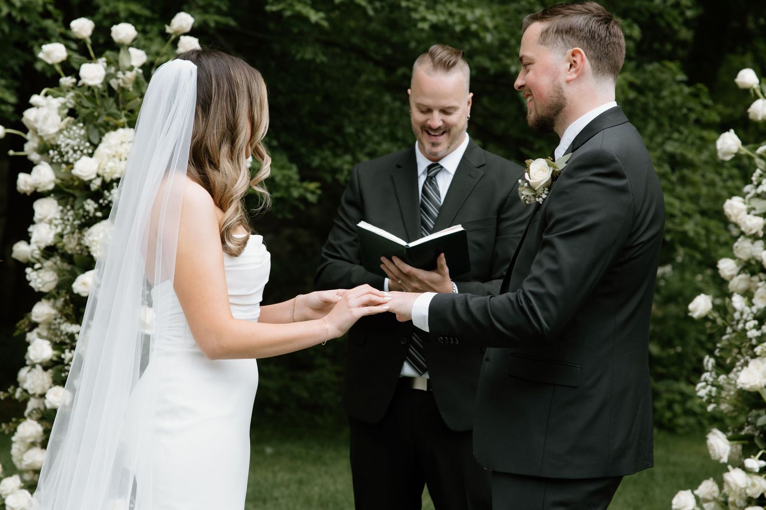 Wedding ceremony in progress with white floral arrangements and guests gathered outdoors.