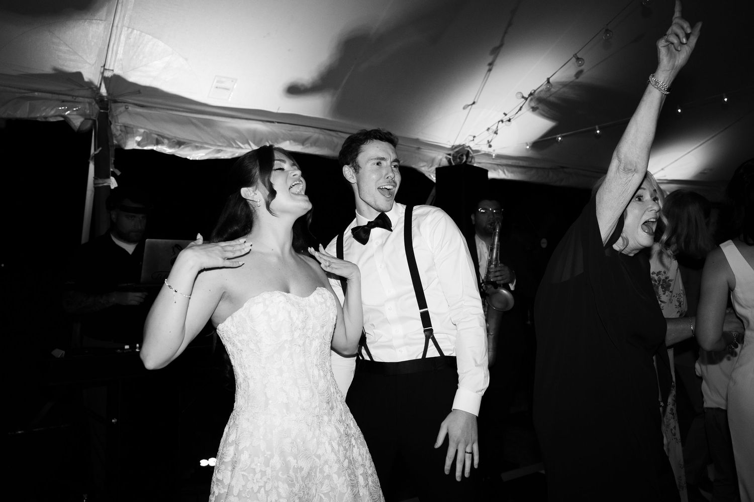 Black and white photo of a bride and groom dancing joyfully at their wedding reception under a tent.