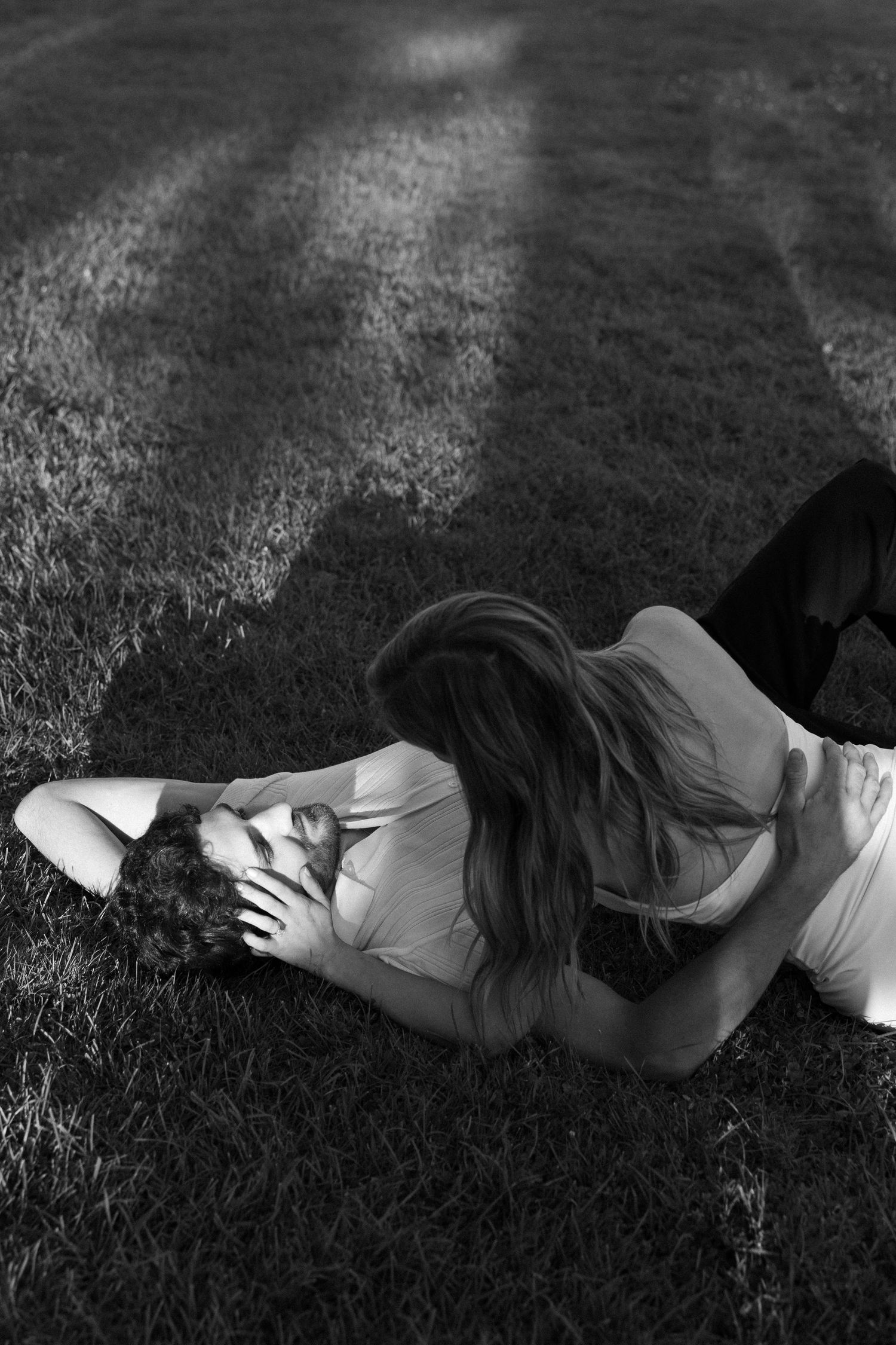 Black and white photo of a woman lying on grass, hair flowing, in a contemplative pose with dramatic shadows.