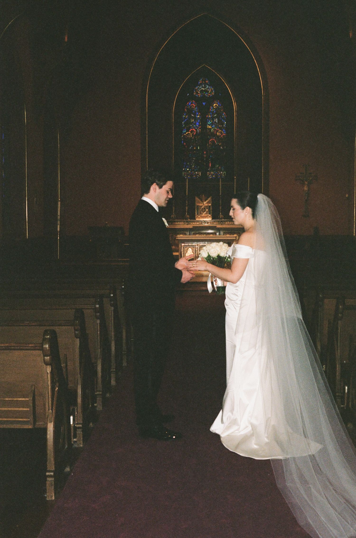 A bride and groom exchange vows at the altar of a traditional church with stained glass windows and wooden pews.