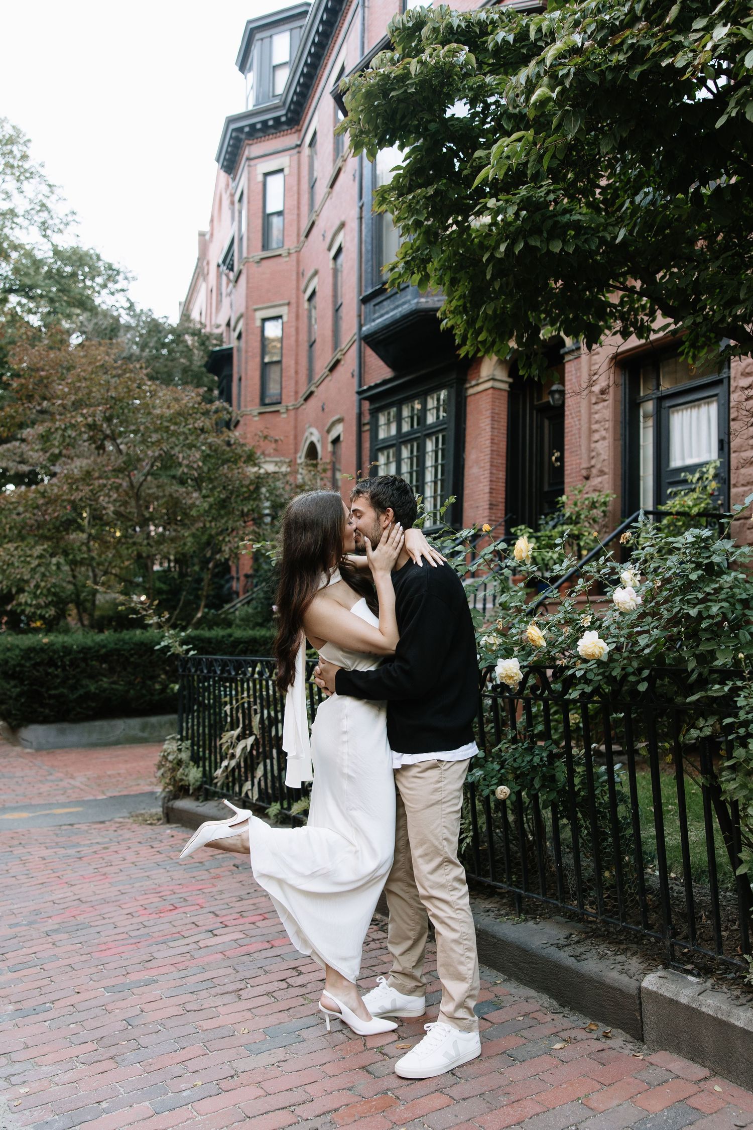 Romantic couple embracing outside brick brownstone with wrought iron fence.