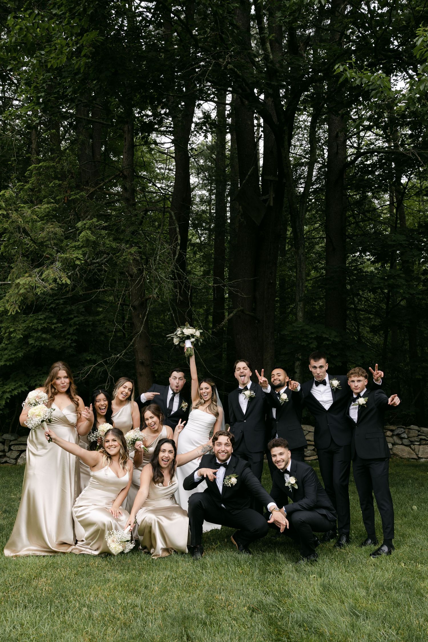 Wedding party lounges casually on grass for fun group photo.