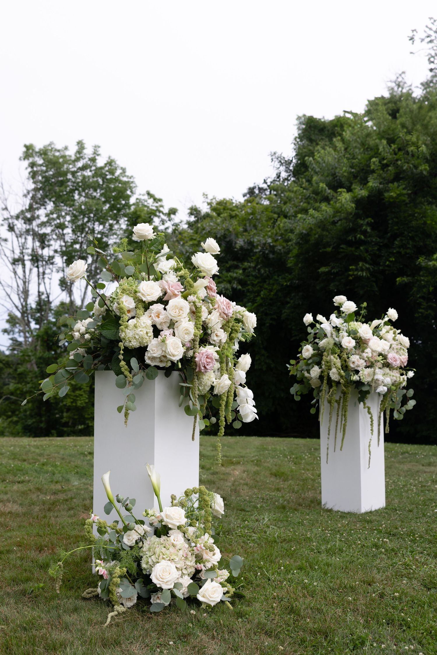White floral arrangements in modern pedestals displayed on grassy outdoor setting.