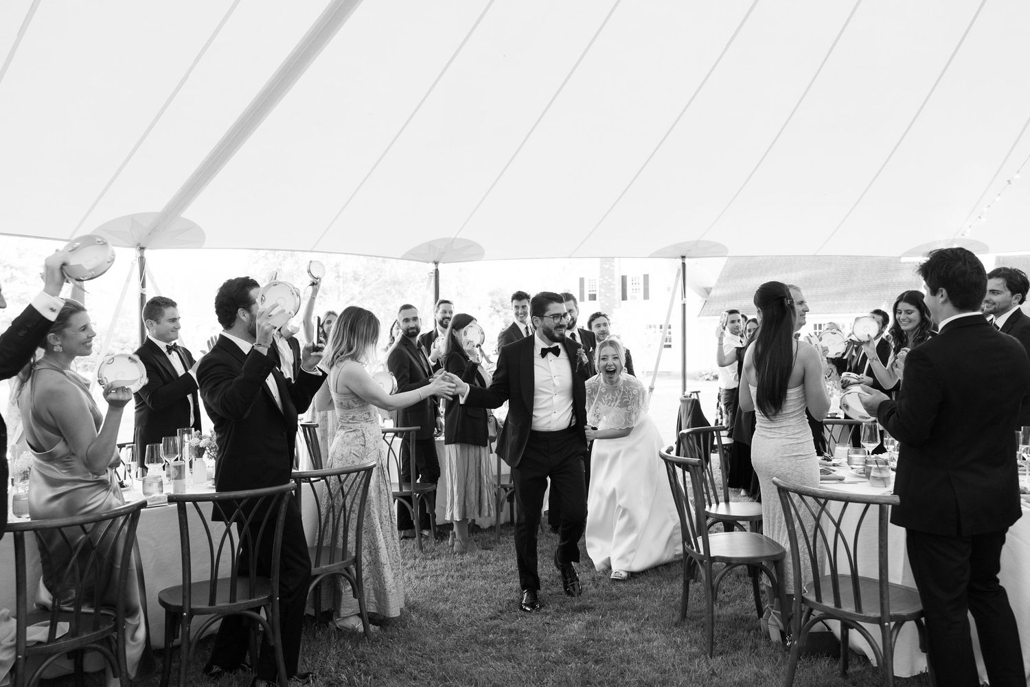 Black and white photo of a bride and groom making a grand entrance at their elegant tented wedding reception.