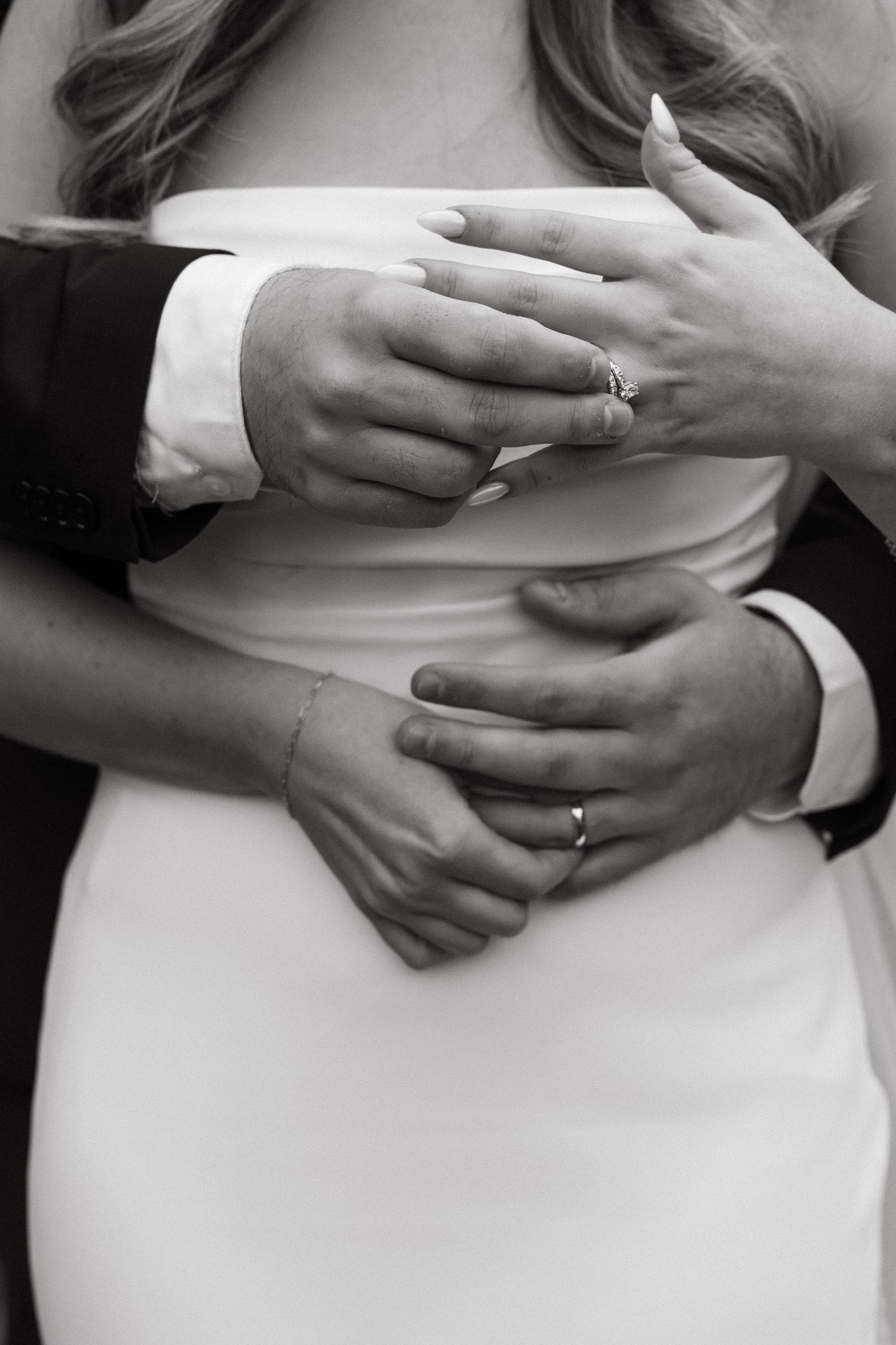 Black and white close-up of hands with wedding rings in intimate embrace.