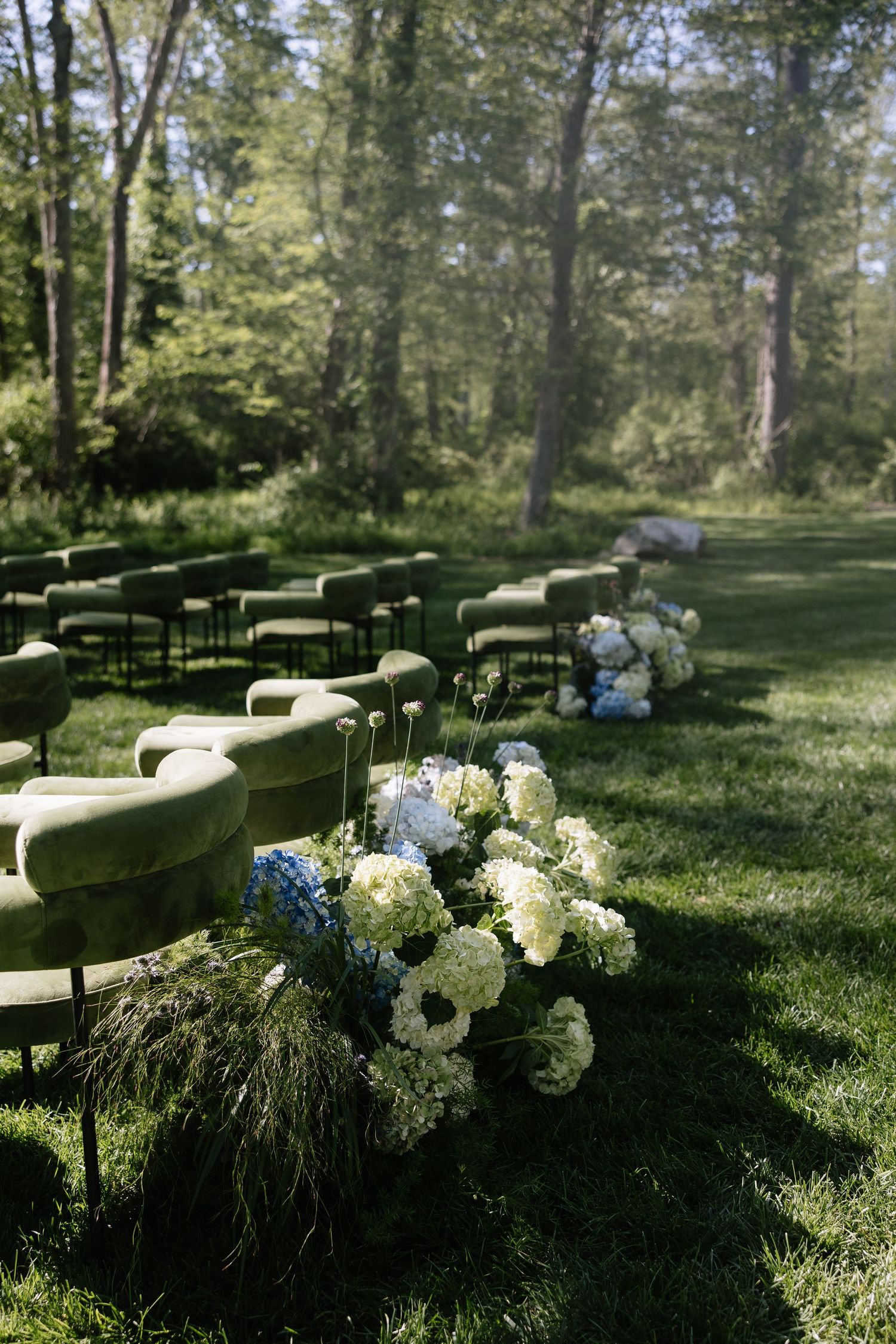 Elegant outdoor wedding seating decorated with white hydrangea arrangements in a wooded setting.