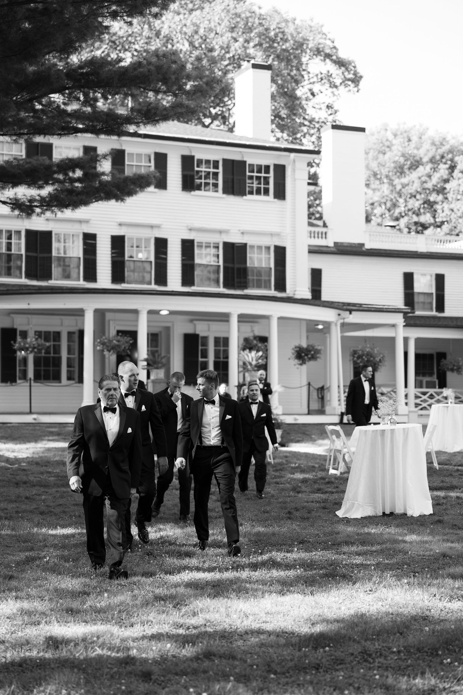 Black and white photo of groomsmen walking from white colonial mansion.