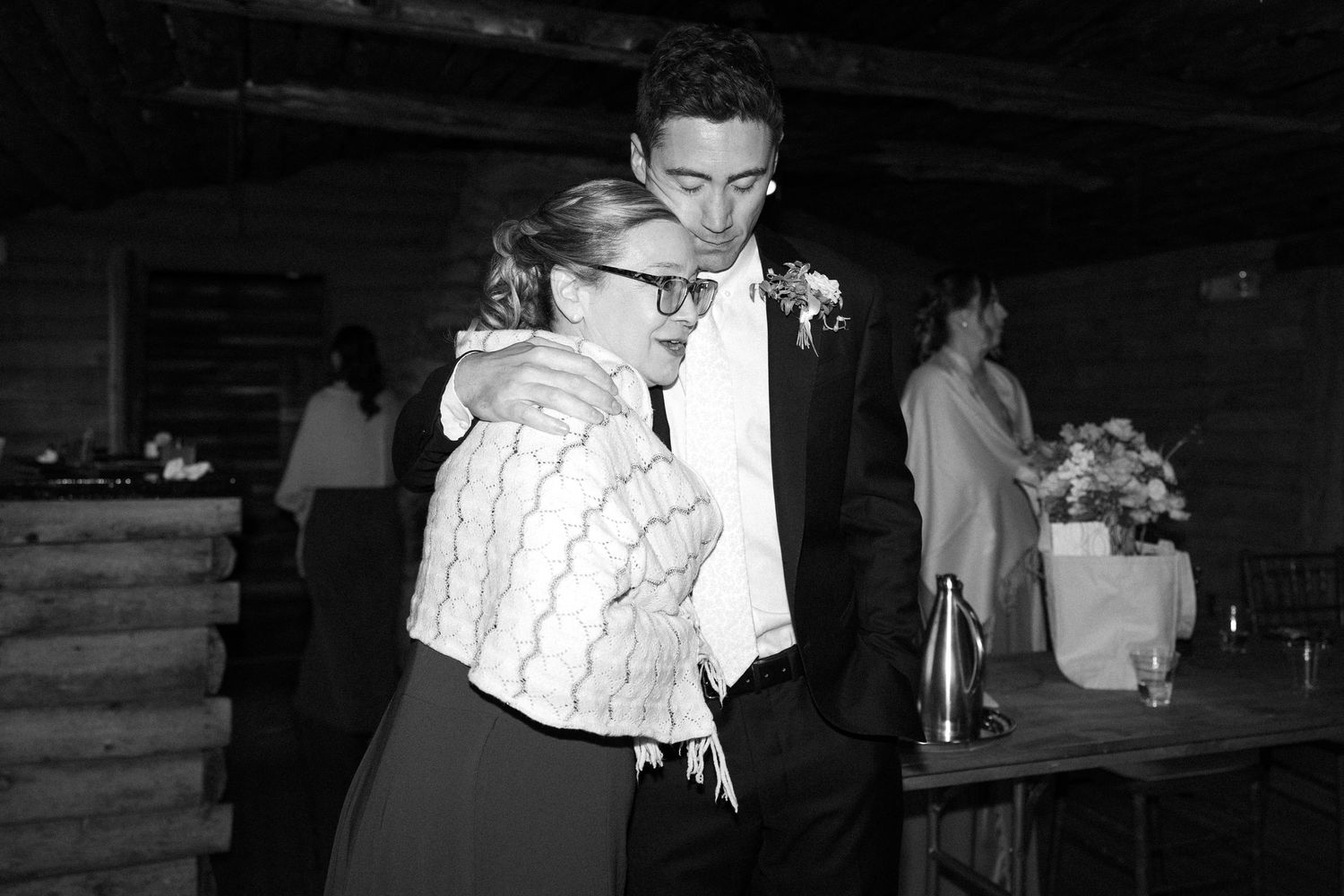 Black and white photo of a couple embracing and dancing at a rustic wedding reception venue.