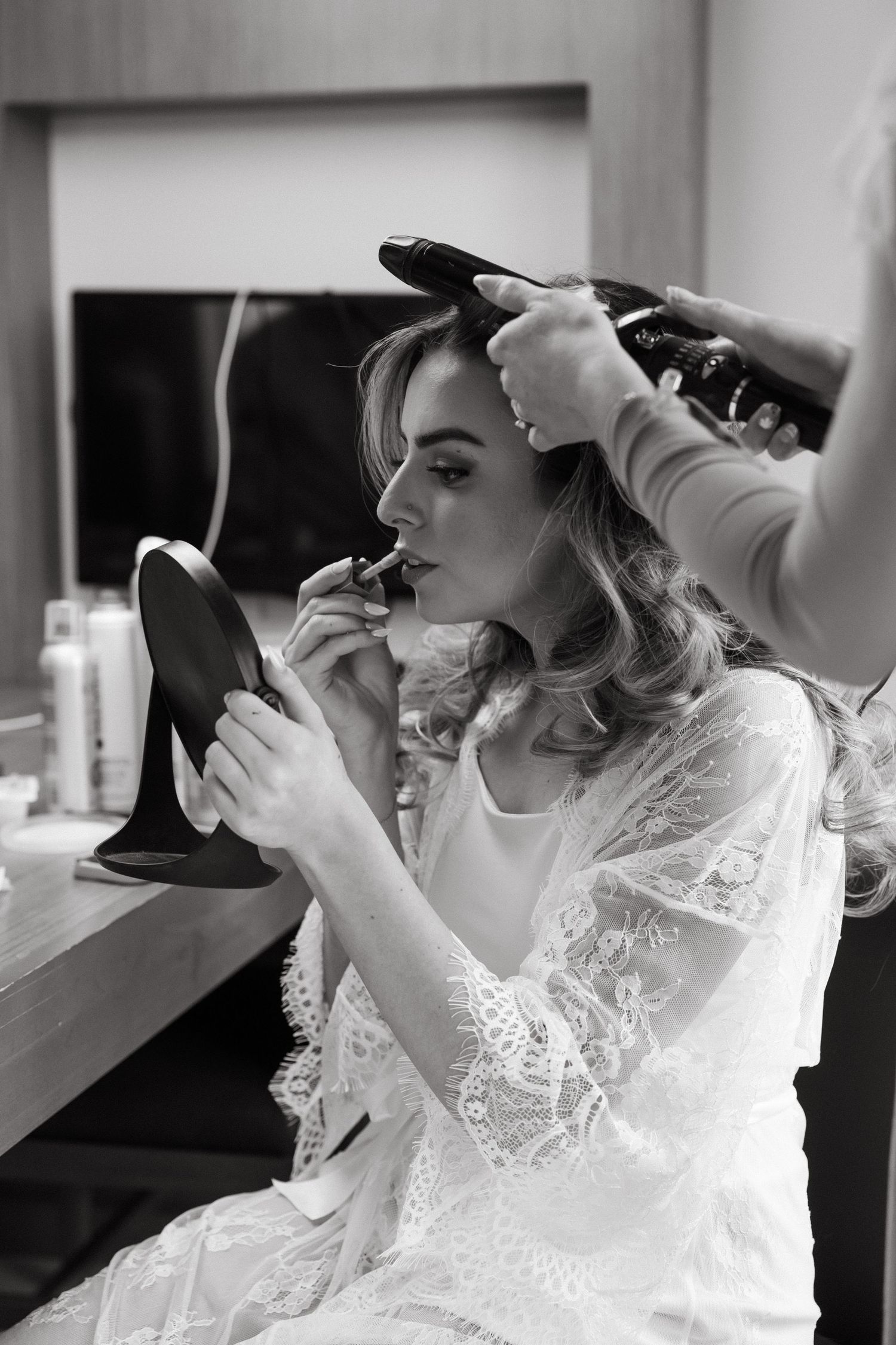 Bride in white lace getting her makeup done during wedding preparations.