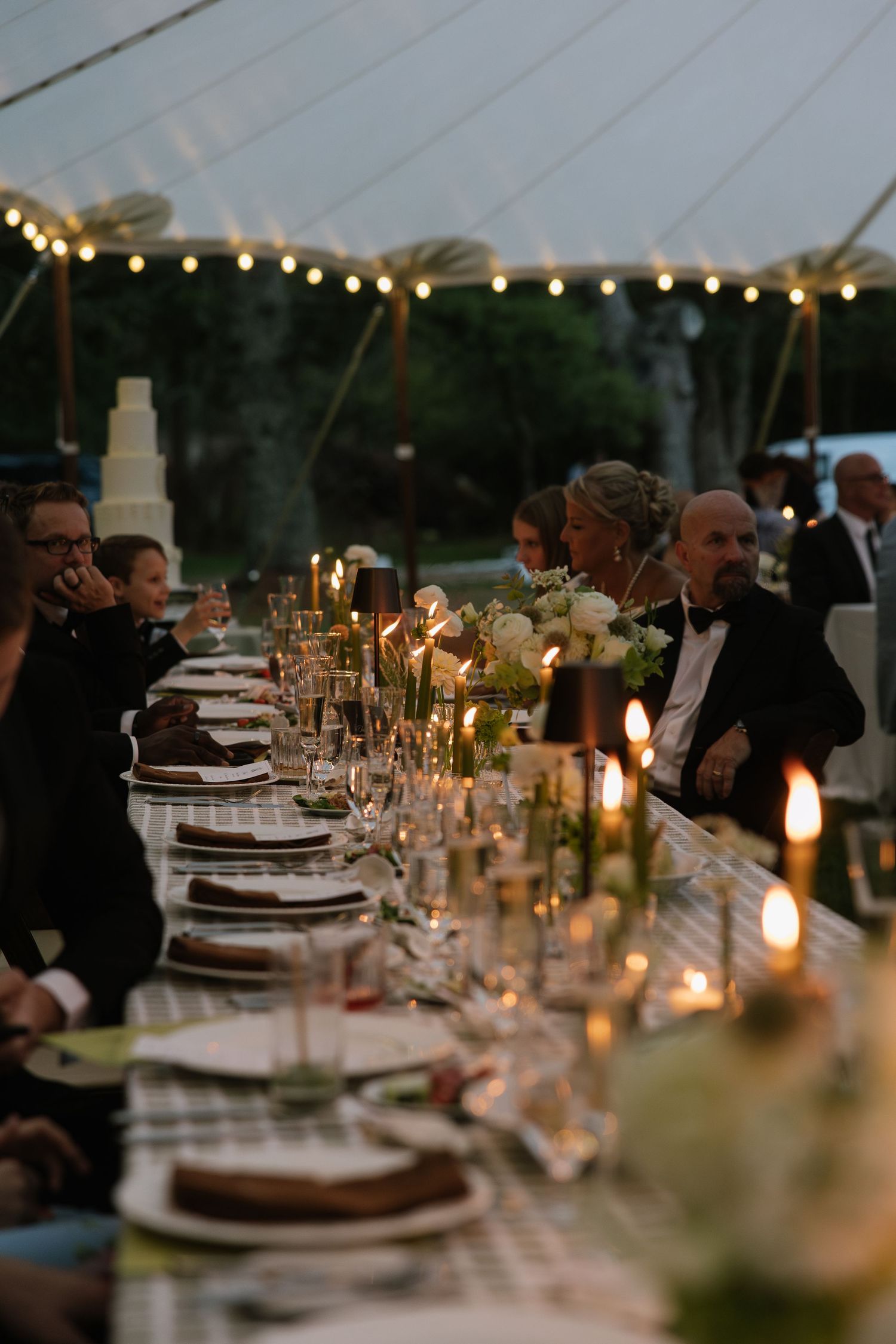 Candlelit wedding reception tables decorated with formal place settings at dusk.