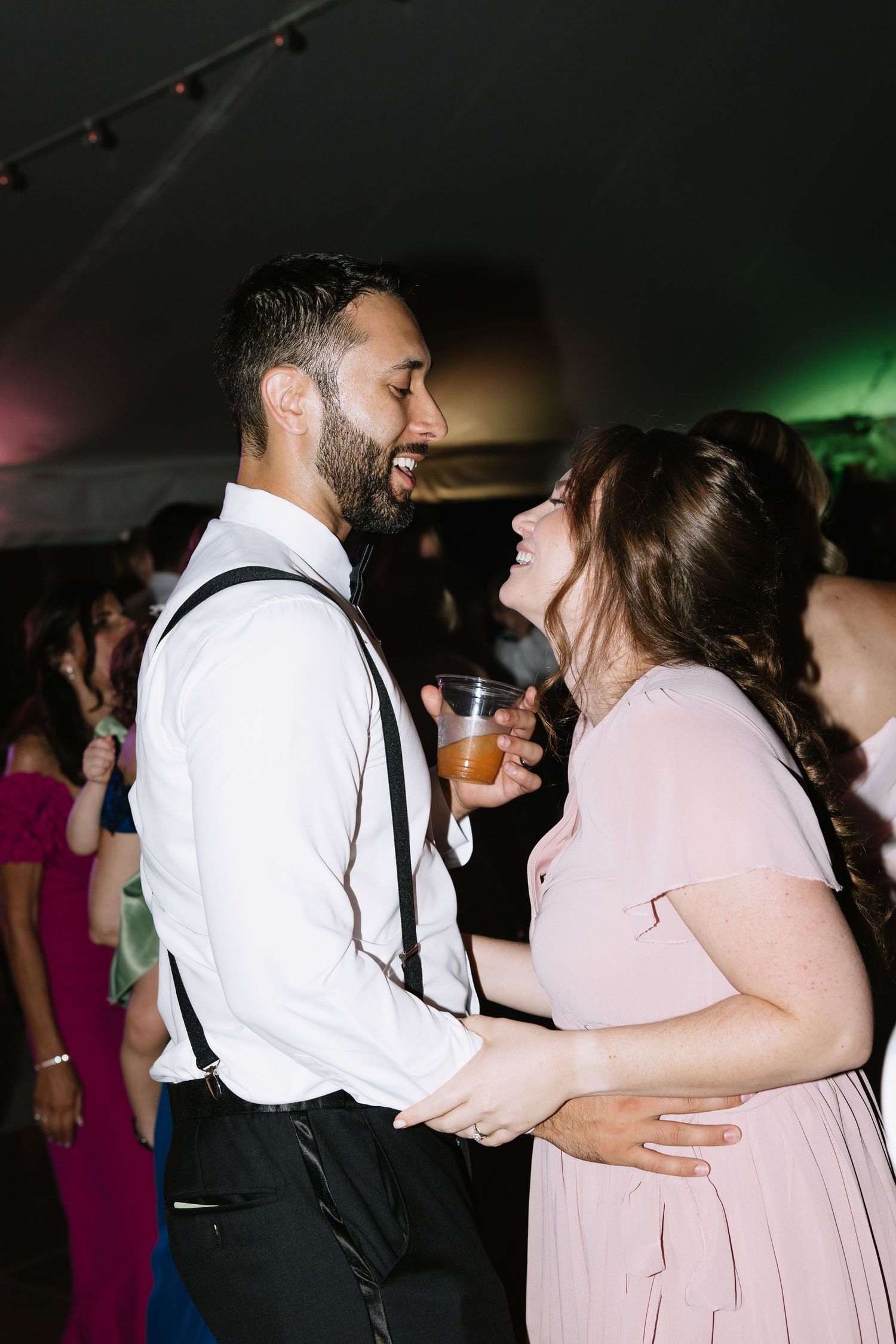 Wedding guests dancing together at a reception party under dimmed lighting.