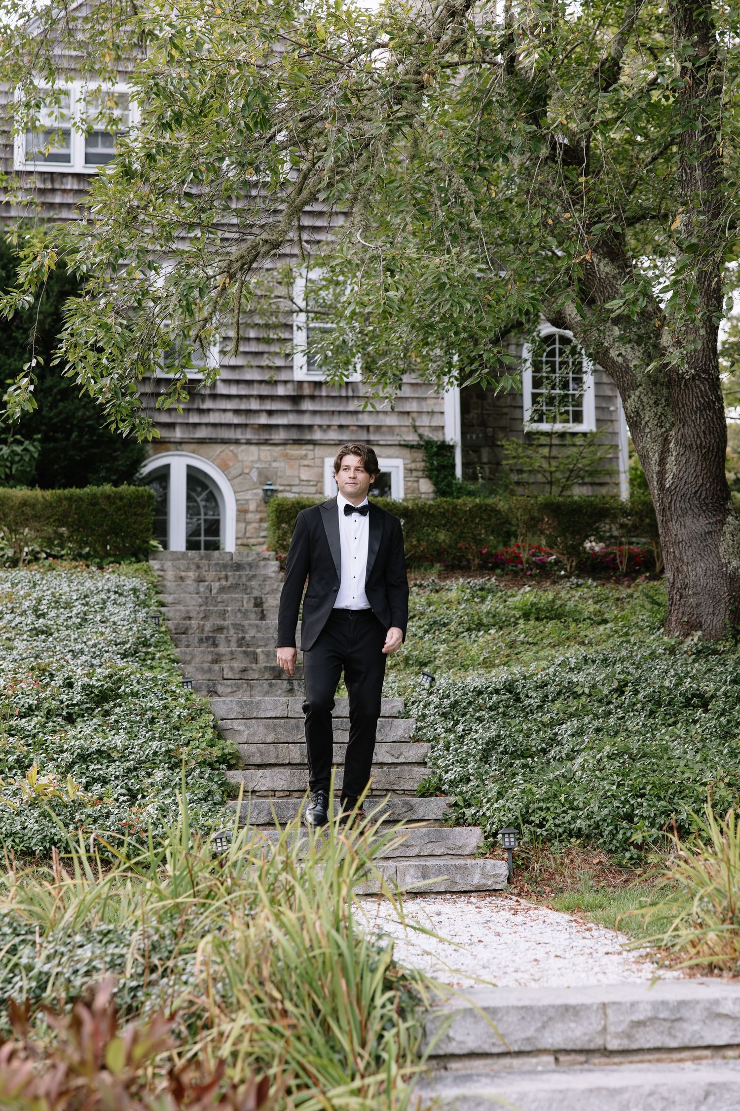 Formal couple walking along a garden path near a stone building.