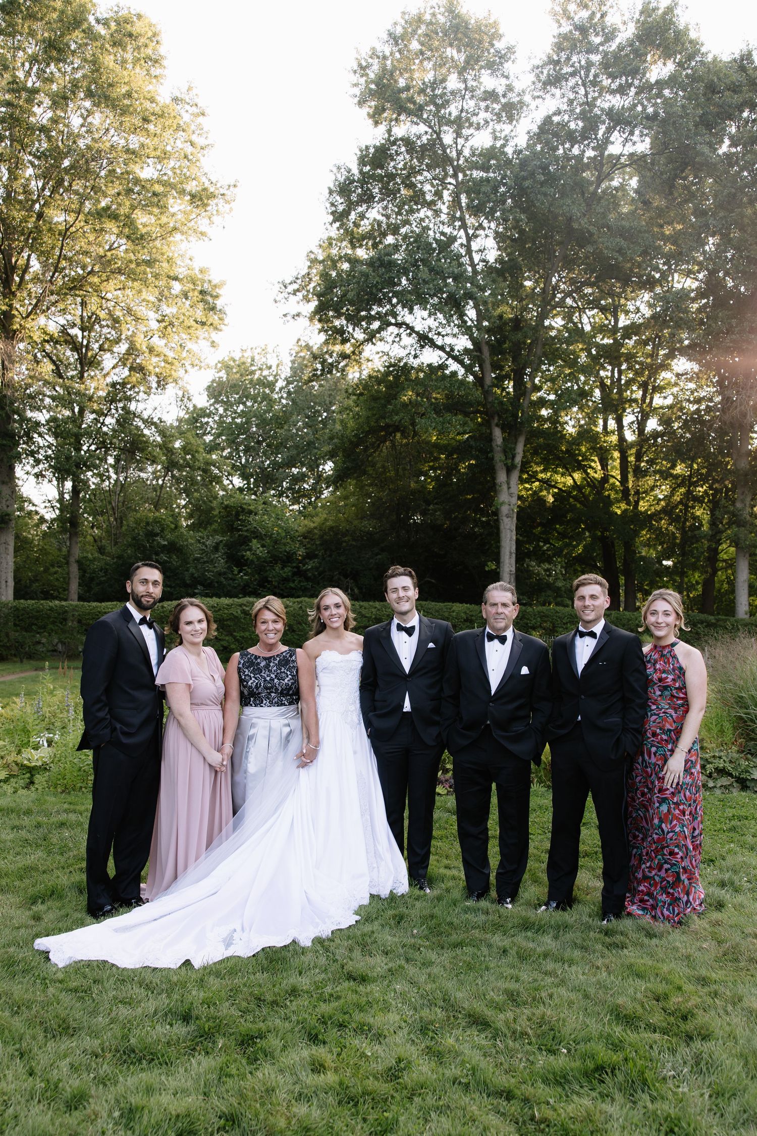 Wedding party poses for formal group photos on a lush green lawn at sunset.