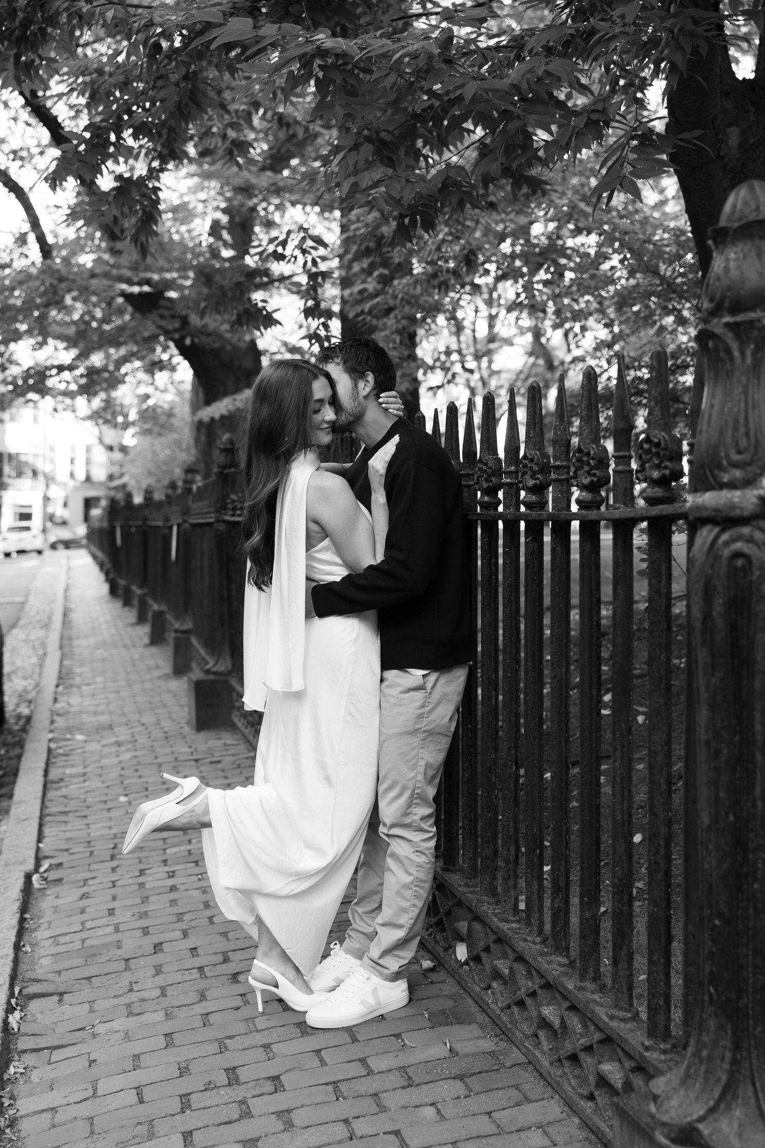 Black and white photo of a couple sharing an intimate moment against a decorative iron fence.
