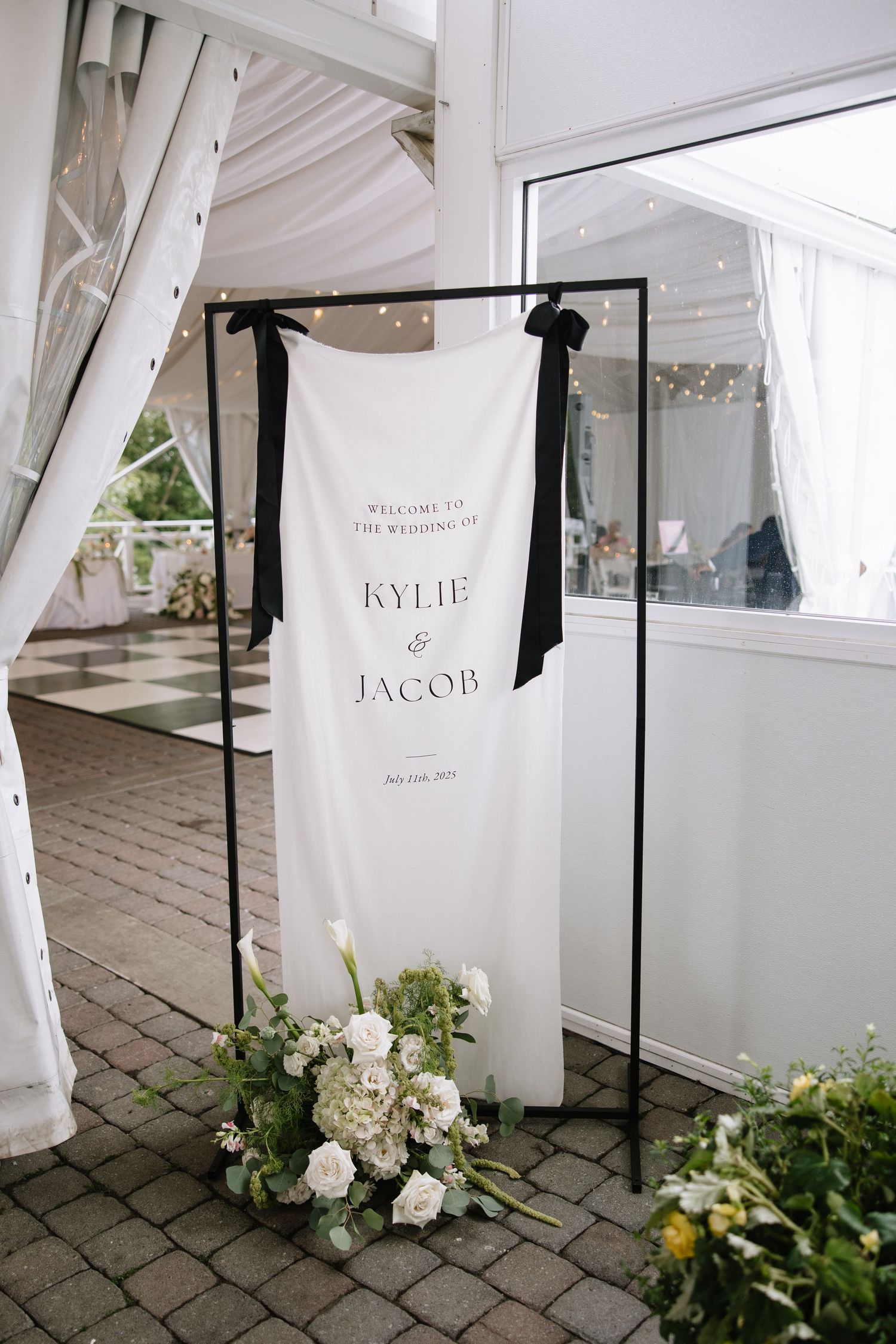 Wedding welcome signs with names displayed on black stands with white floral decorations.