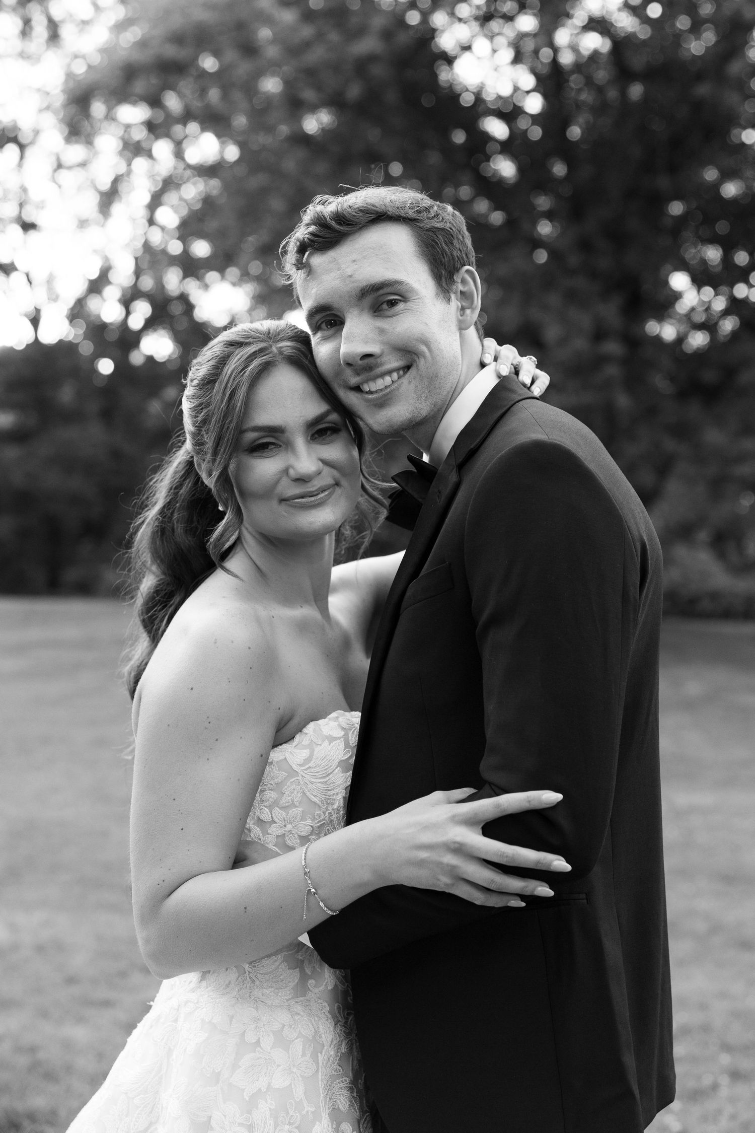 Black and white photo of a smiling bride and groom embracing outdoors on their wedding day.