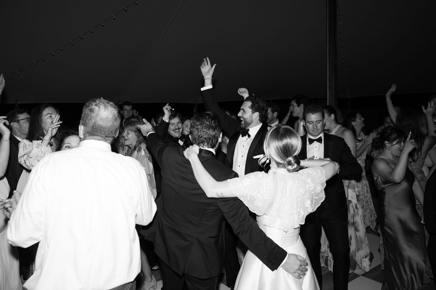 Black and white wedding reception dance floor photo with bride, groom, and guests celebrating joyfully.