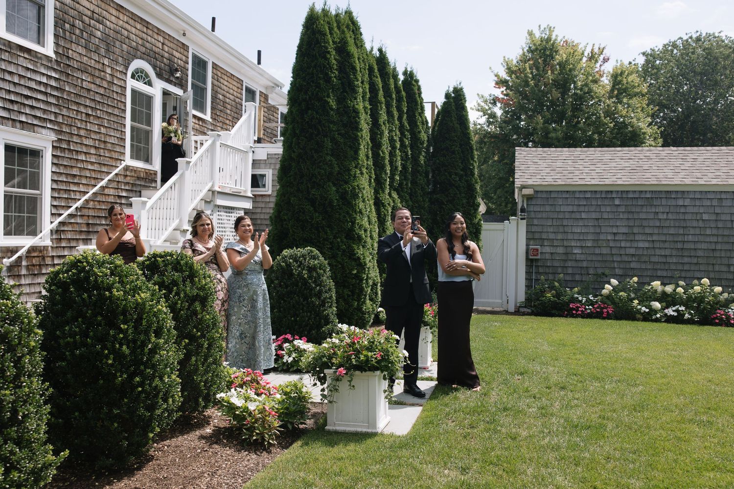 Wedding party gathers outside historic New England venue on sunny day.