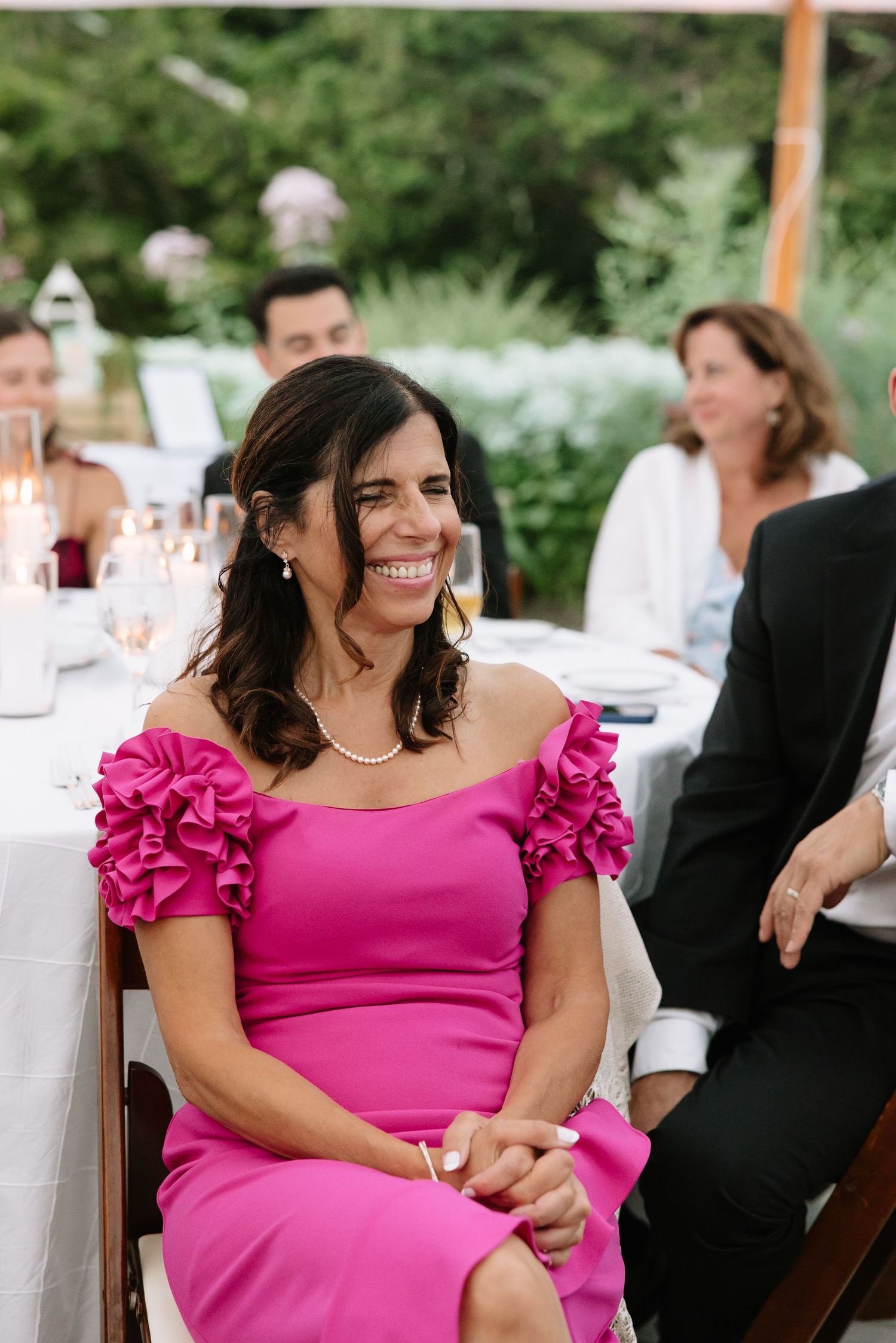 A guest in a vibrant pink dress laughs during a wedding reception.