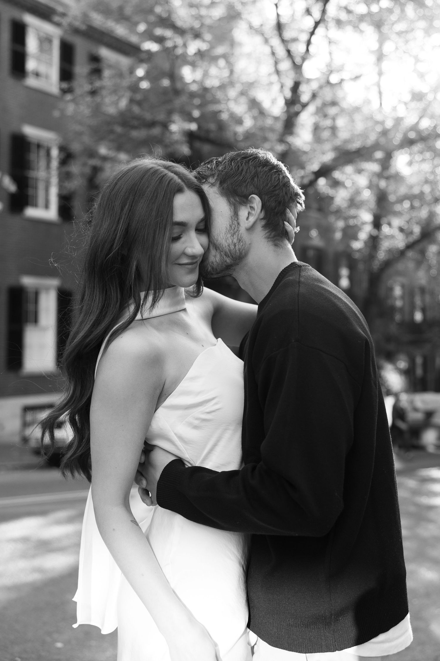 Black and white portrait of a couple sharing an intimate moment in front of historic architecture.